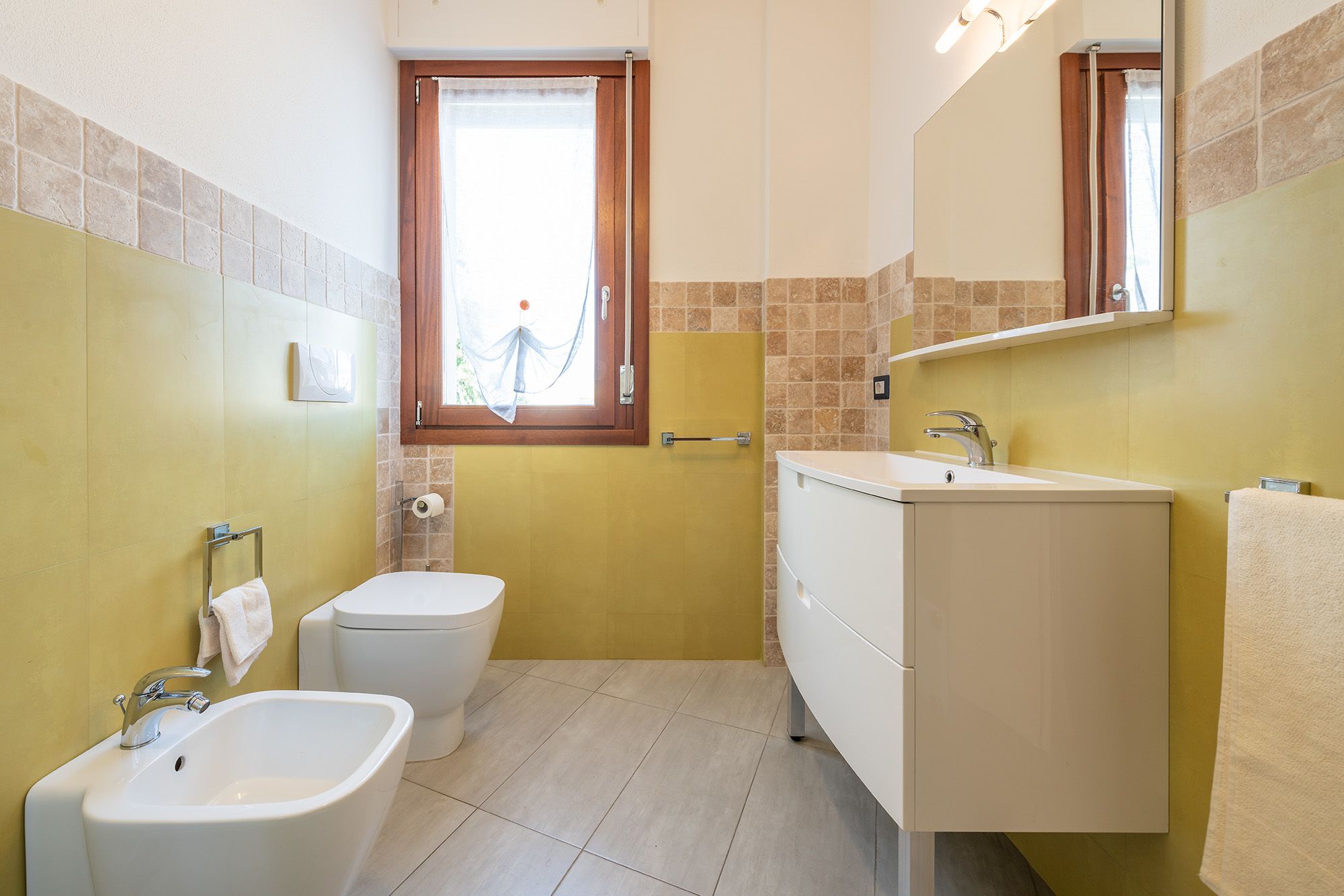 A compact bathroom with a toilet, bidet, sink, and a mirror above the sink.