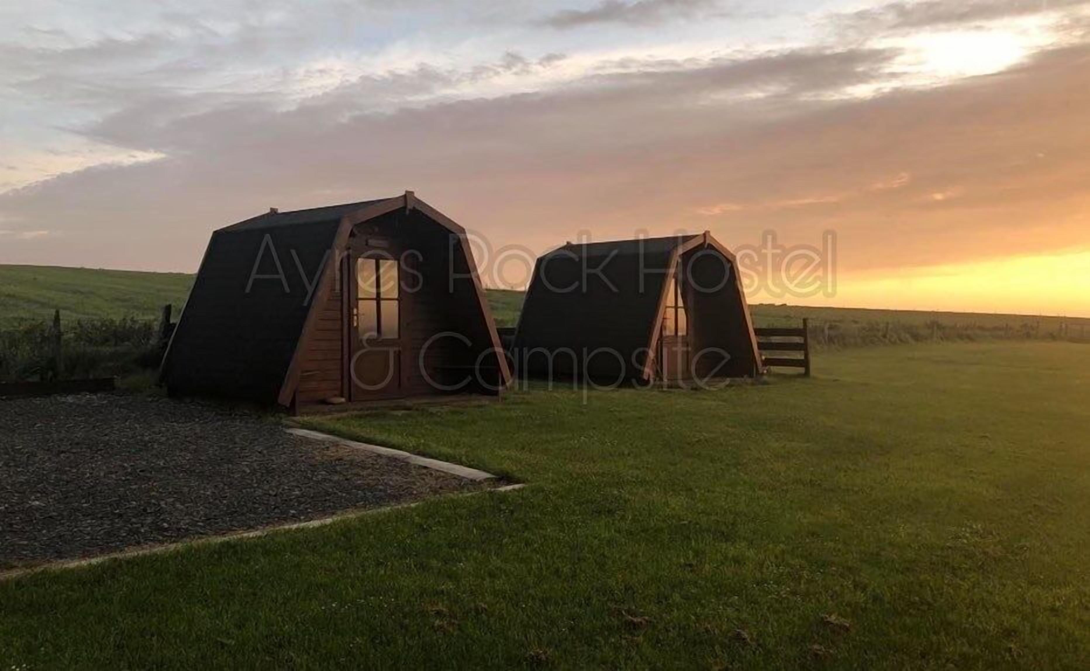 Dos tiendas de campaña del Aylesbury Rock Hotel en un campo de hierba, con un atardecer al fondo.