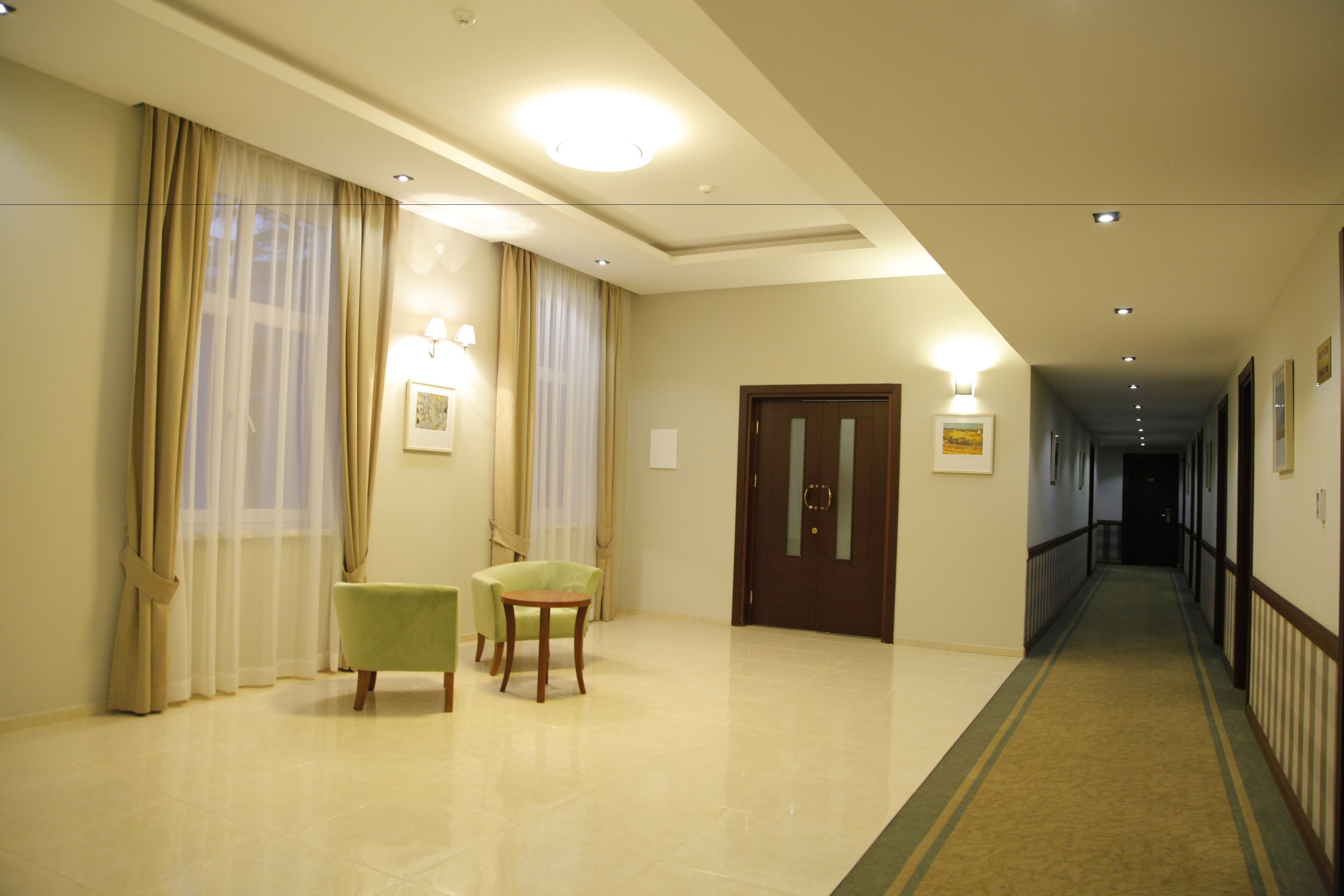 A hotel corridor with a carpeted floor, a wooden door, and two chairs.
