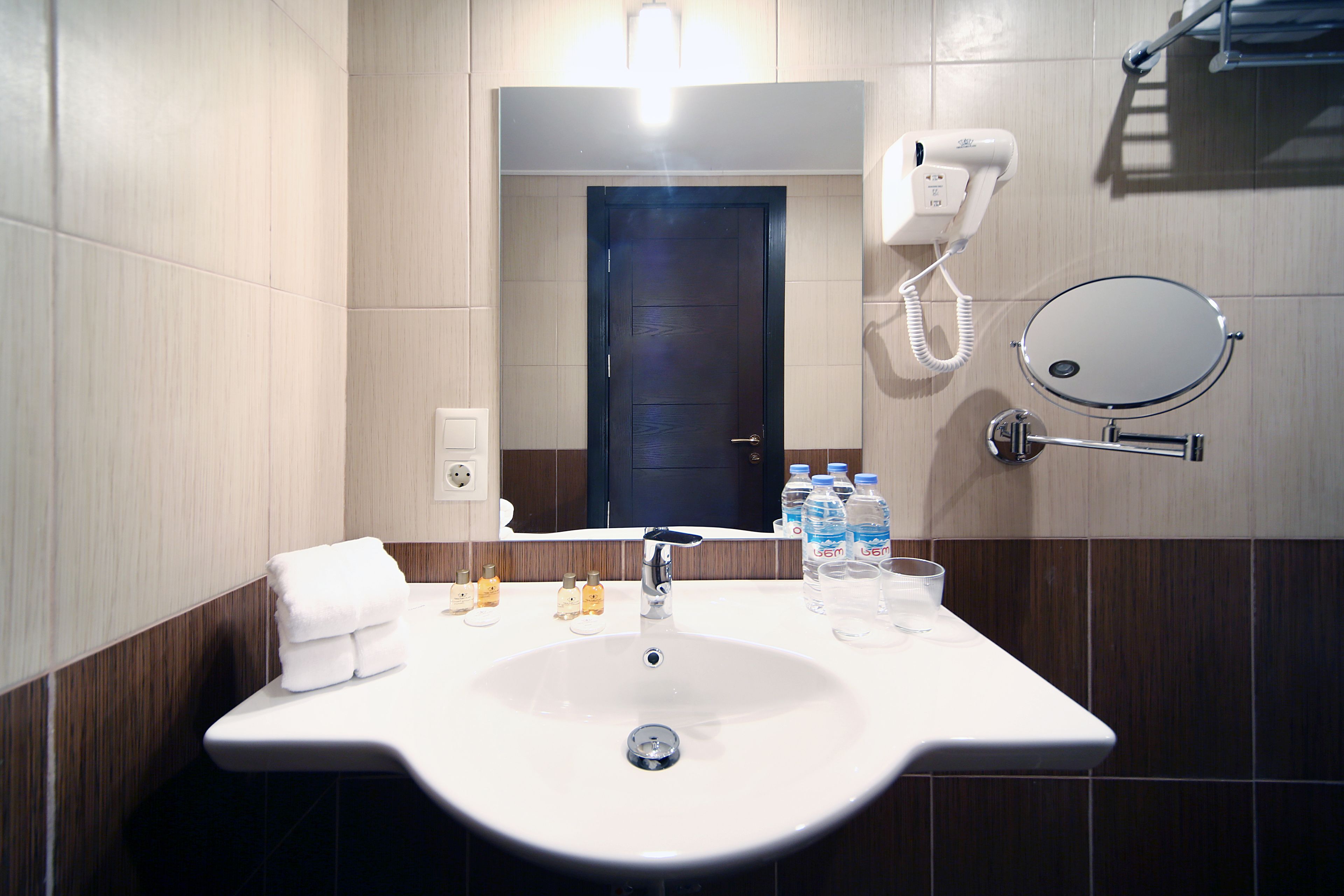 Un baño con lavamanos blanco, espejo, secador de pelo y artículos de aseo.