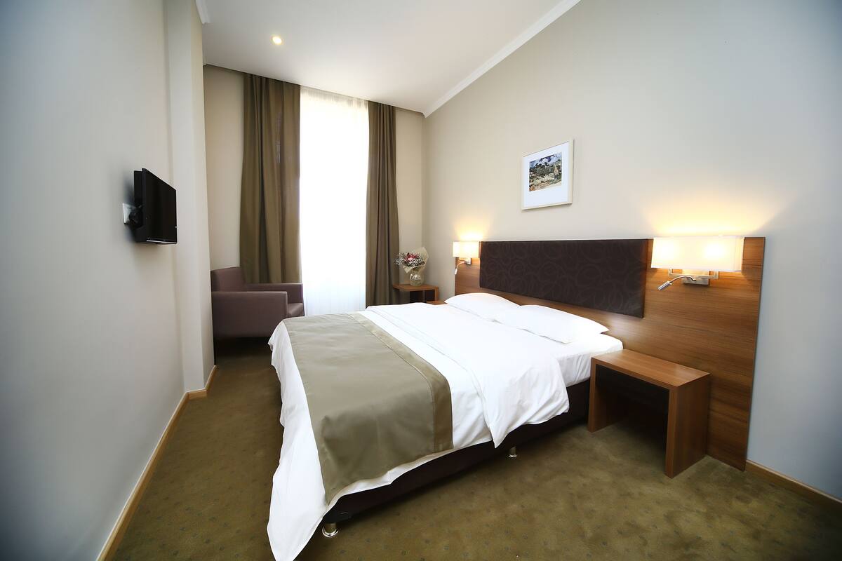 Une chambre d’hôtel équipée d’un lit, d’une table de chevet, d’une lampe et d’un téléviseur à écran plat fixé au mur.