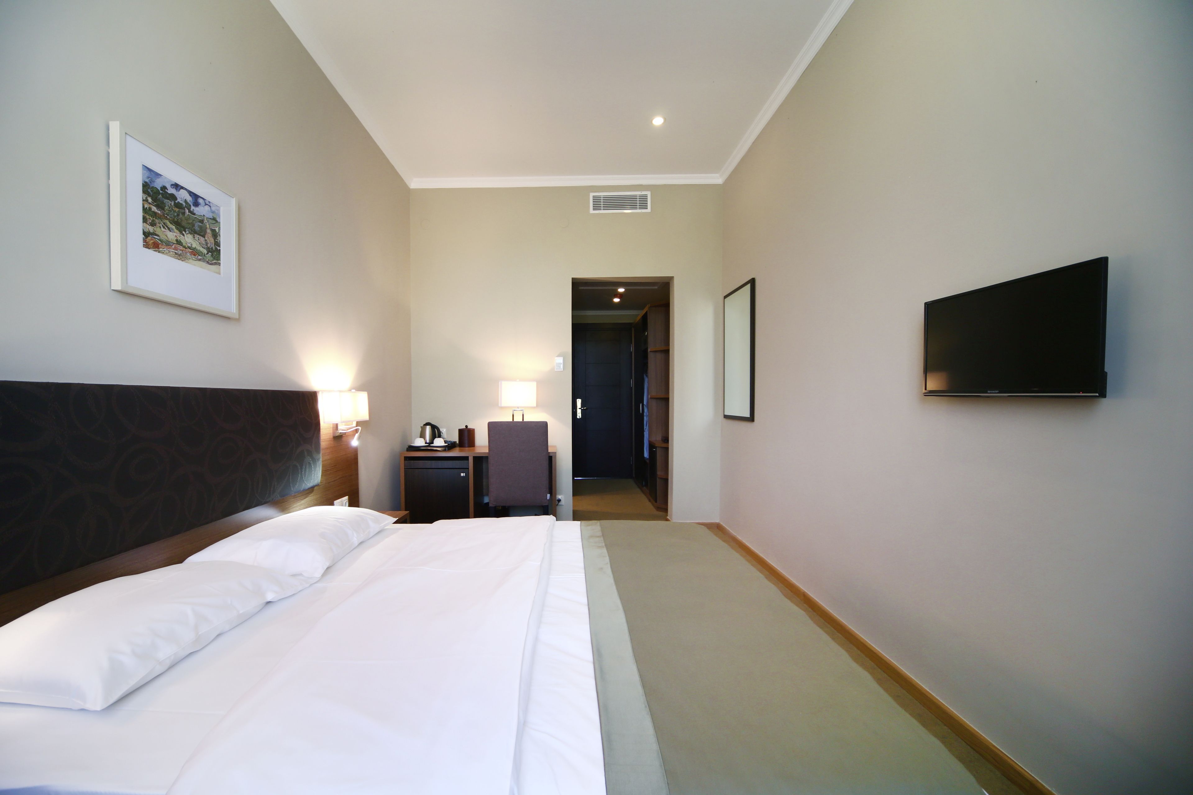 A hotel room with a bed, a desk, a chair, a TV, and a framed picture on the wall.
