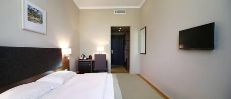 Une chambre d’hôtel avec un lit, un bureau, une chaise, une télévision et un tableau encadré au mur.