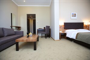 Ein Hotelzimmer mit Bett, Schreibtisch, Stuhl, Sofa und einem kleinen Tisch mit Flasche und Gläsern.