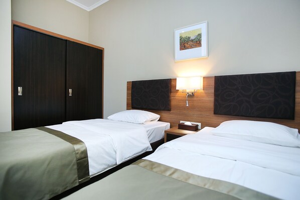 A hotel room with two single beds, a wooden headboard, a nightstand, a lamp, and a wardrobe.