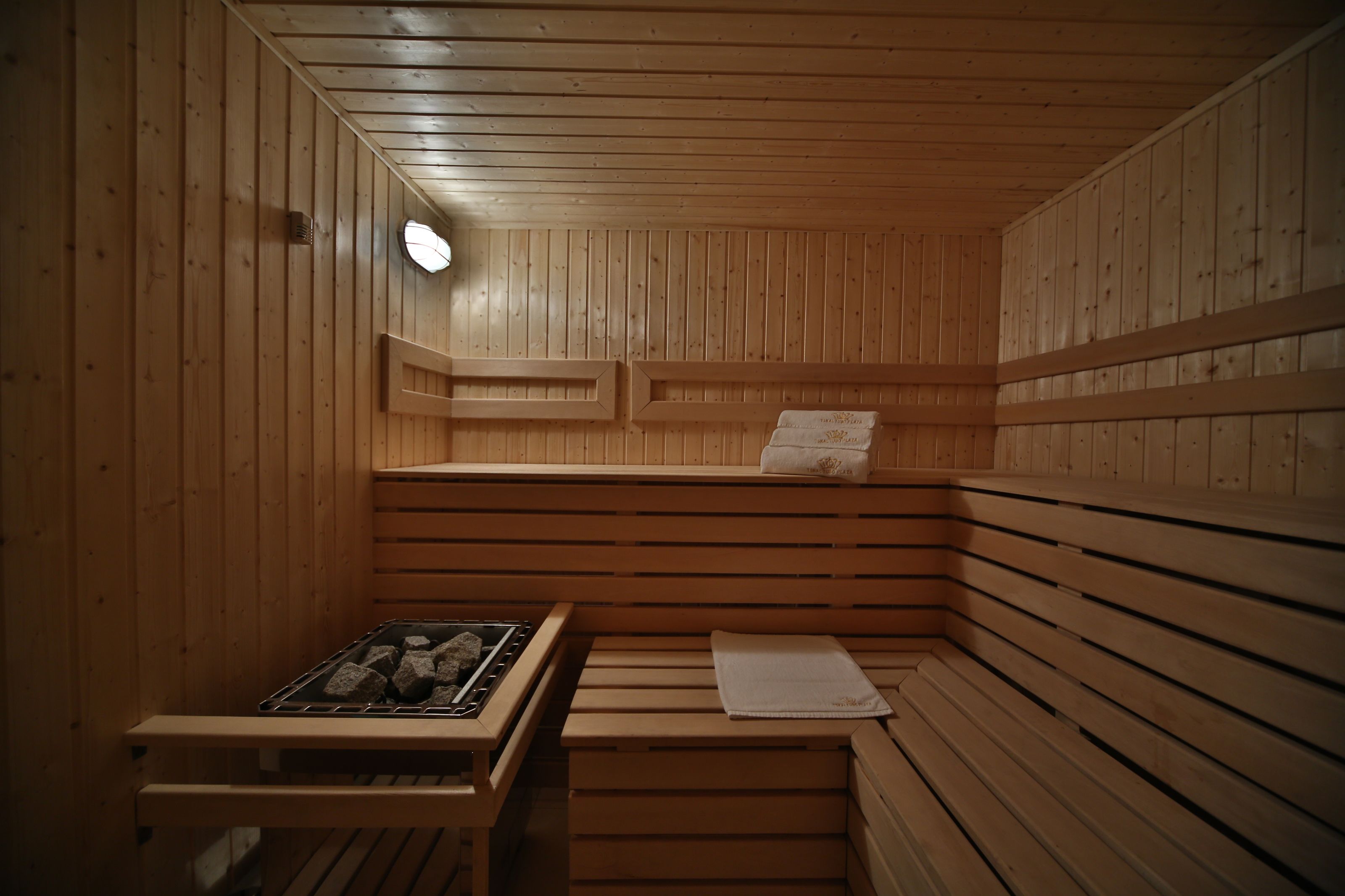 Una sauna con paredes y bancos de madera, un banco con una toalla y un calentador.