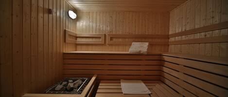 Una sauna con paredes y bancos de madera, un banco con una toalla y un calentador.