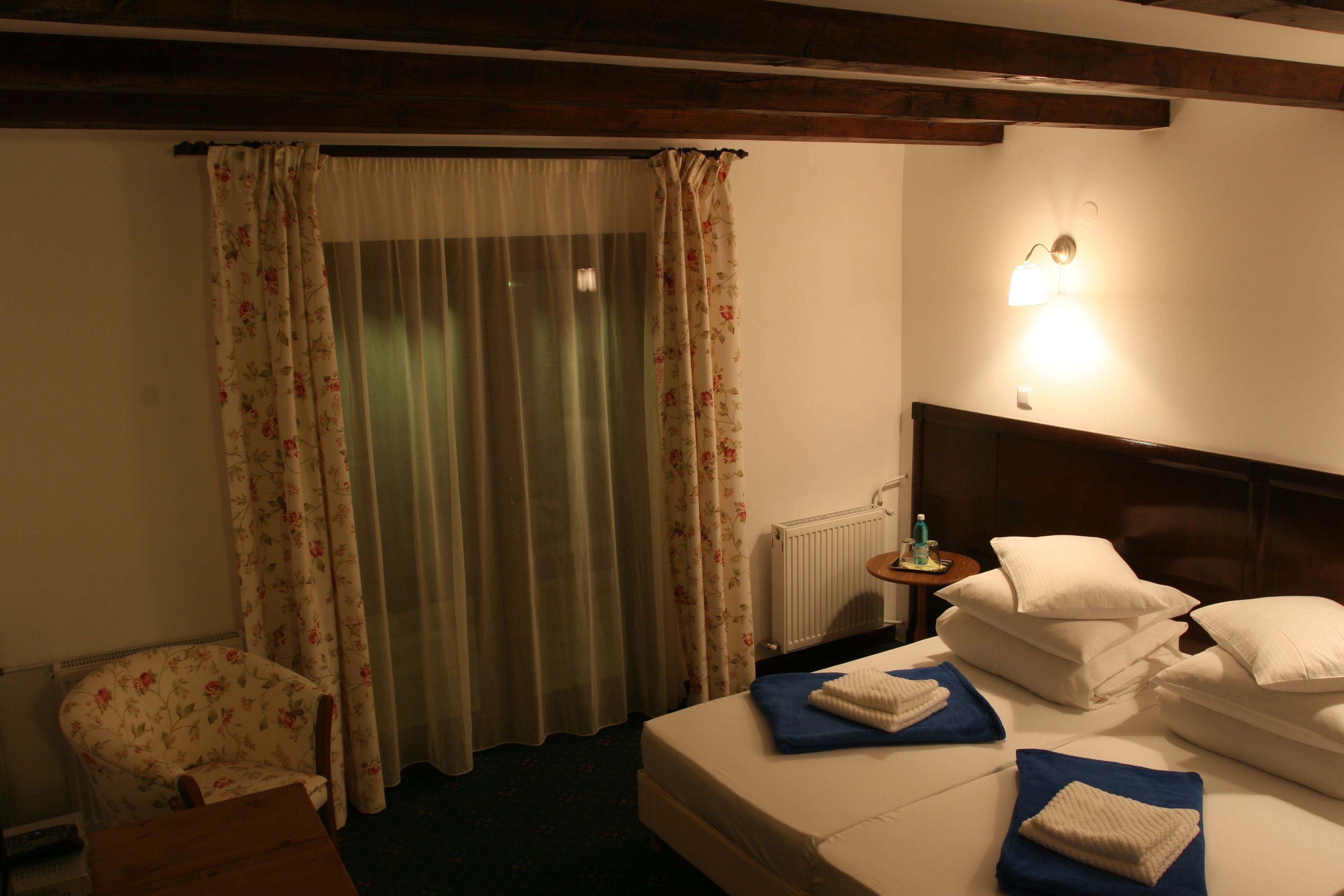 Habitació d'hotel amb un llit, una cadira, una taula, una làmpada i cortines.