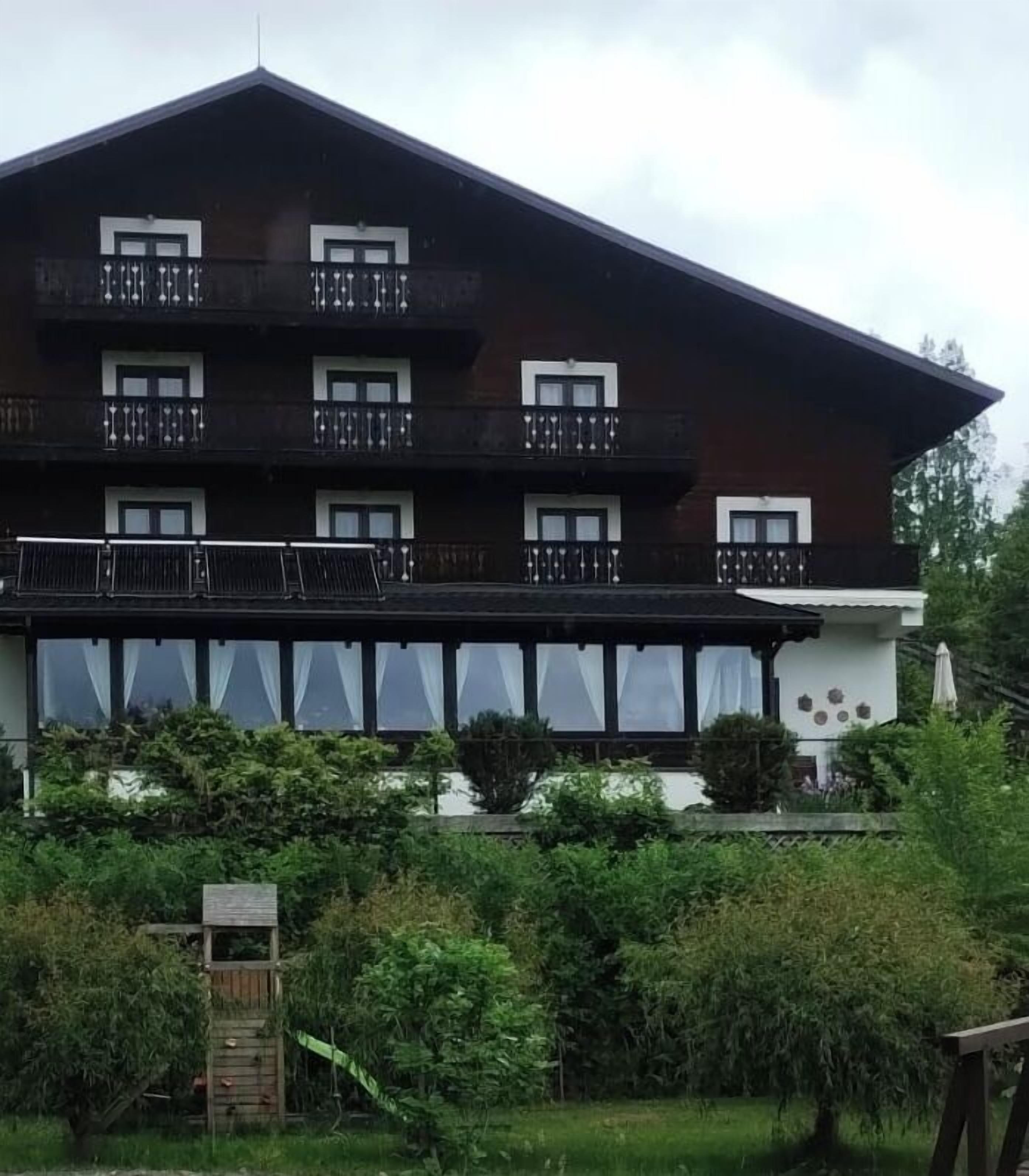A multi-story building with balconies, large windows, and a garden area in front.