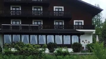 A multi-story building with balconies, large windows, and a garden area in front.