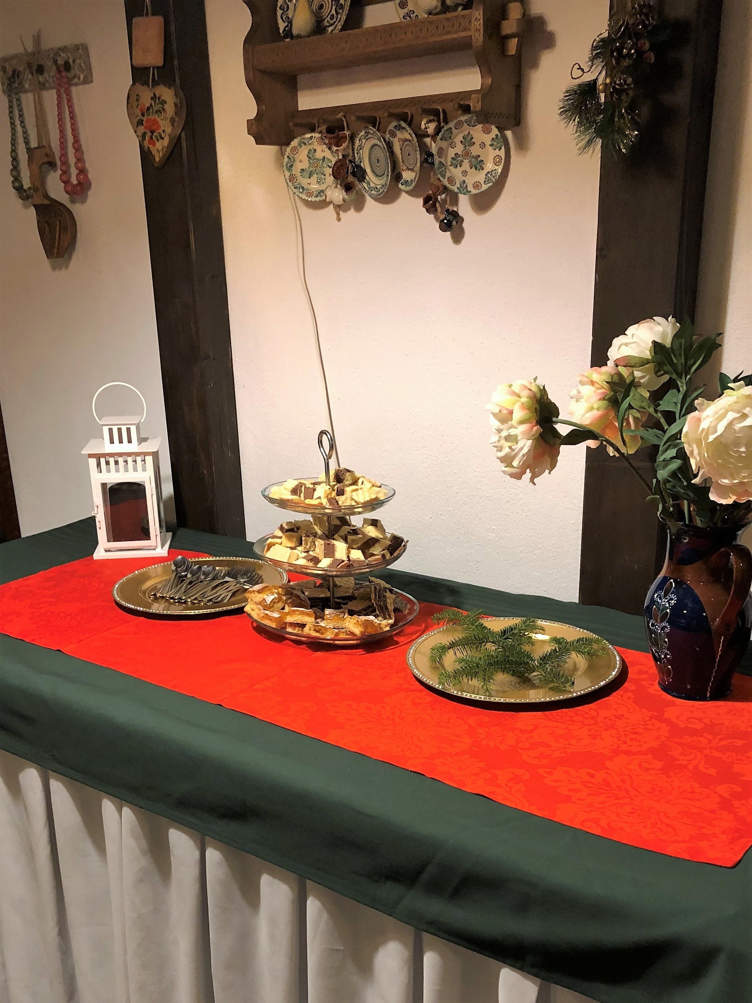 Uma mesa com toalha vermelha, decorada com pratos, um vaso de flores e um candeeiro pendente.
