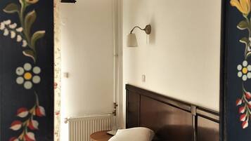 Une chambre à coucher comprenant un lit, une table de chevet, une lampe fixée au mur et un radiateur.