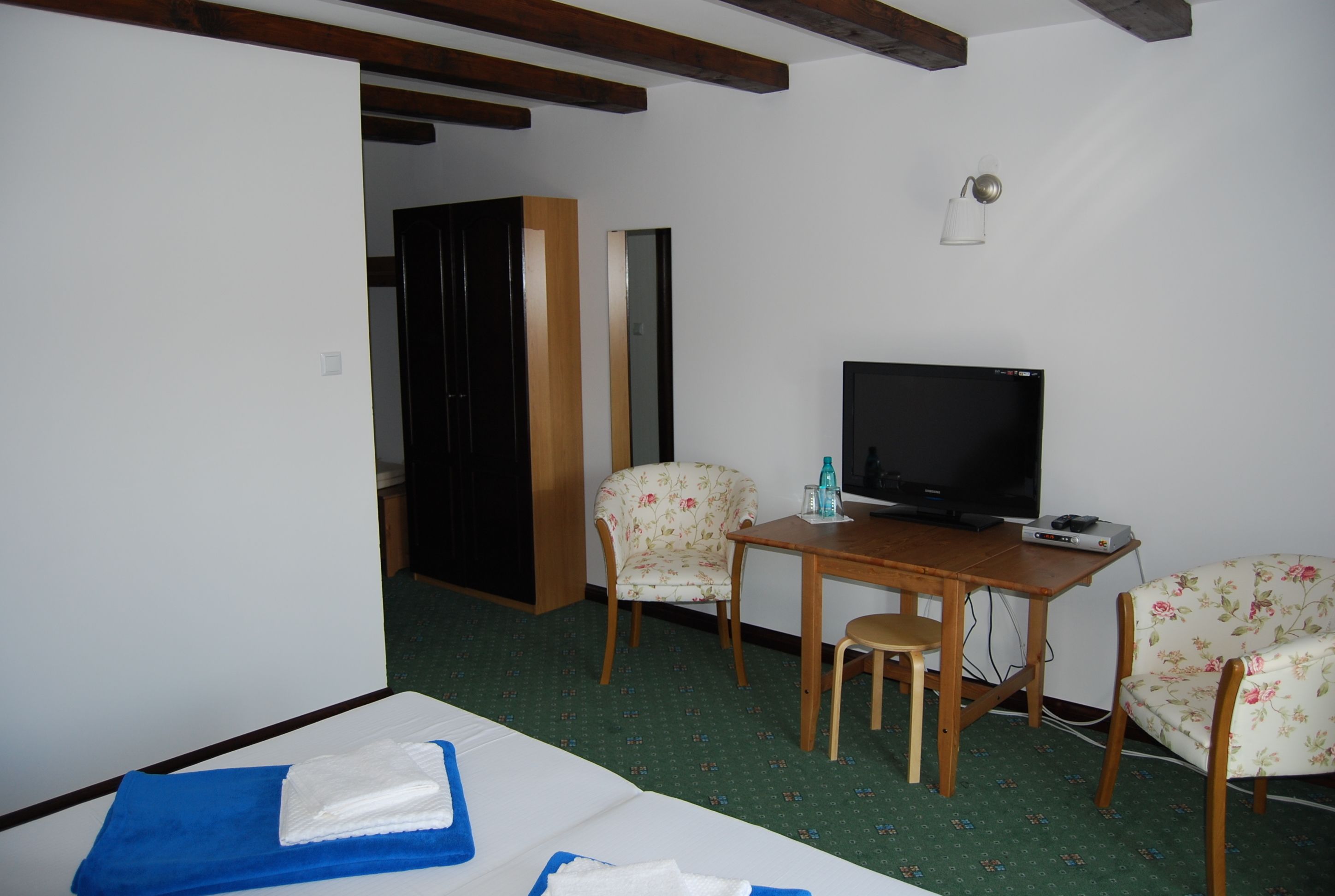 A hotel room with a bed, a desk with a television, two floral chairs, and a wooden wardrobe.