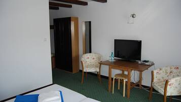 A hotel room with a bed, a desk with a television, two floral chairs, and a wooden wardrobe.