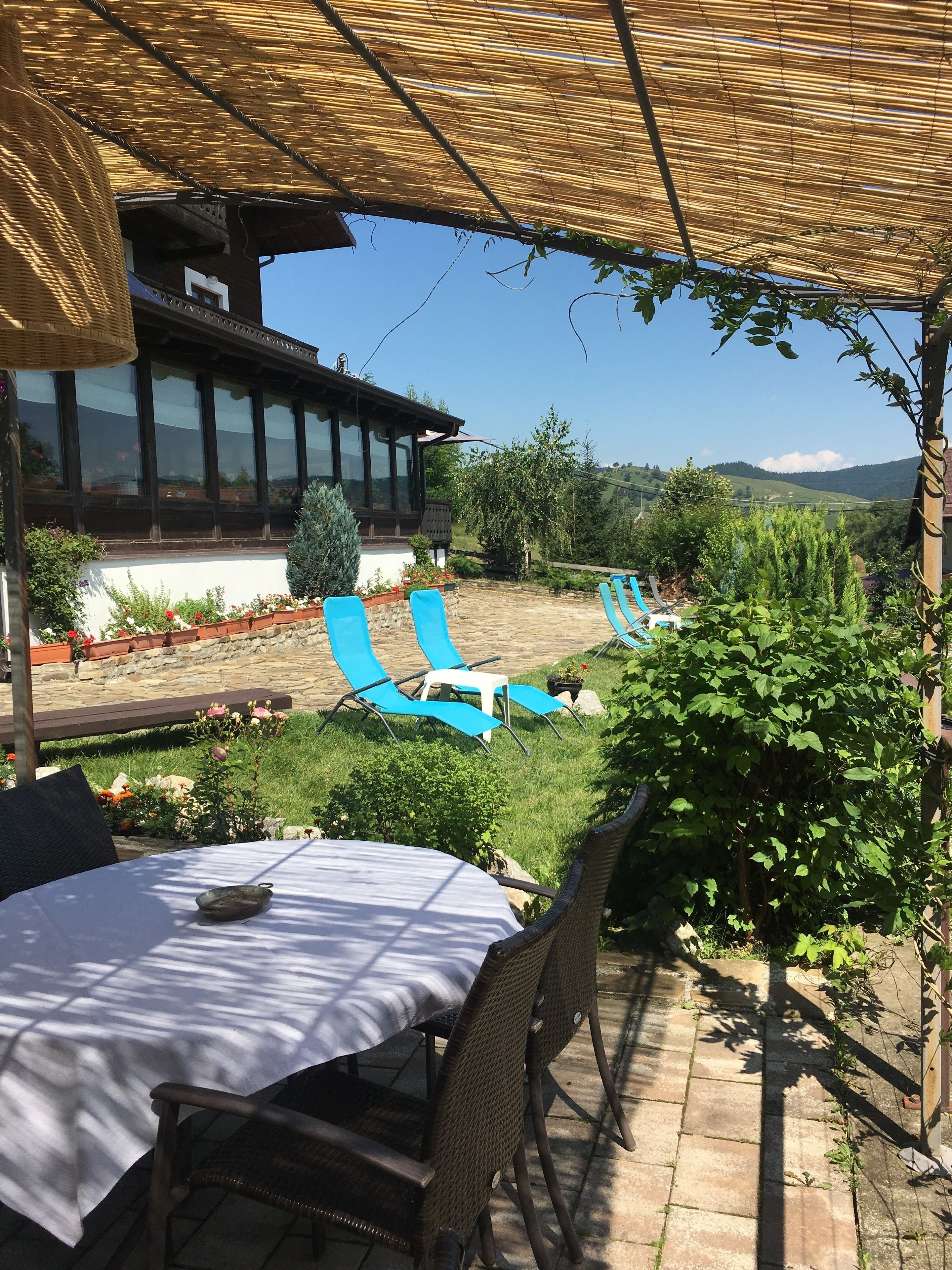 A patio area with a table and chairs, a covered seating area with blue lounge chairs, and a view of a building and hills in the background.