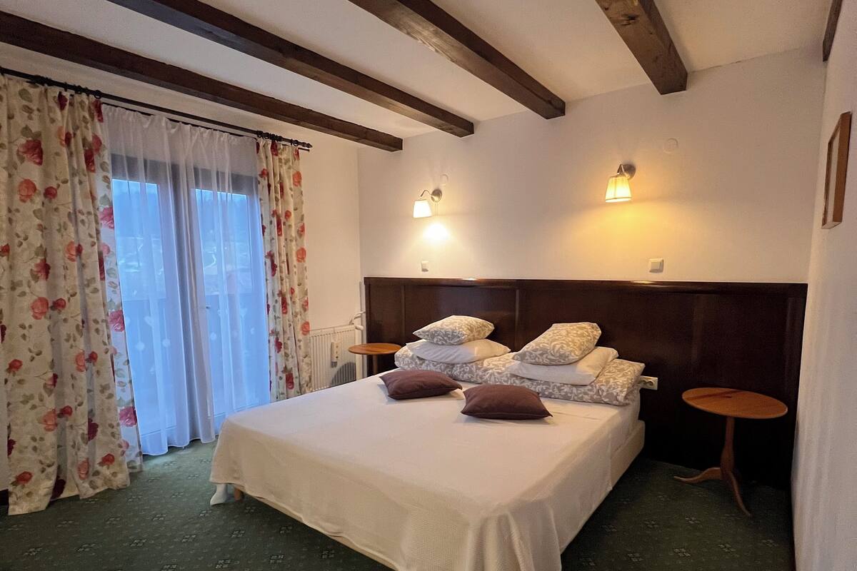 Un dormitorio con una cama, cortinas florales, un cabecero, dos mesitas de noche y una lámpara de pared.