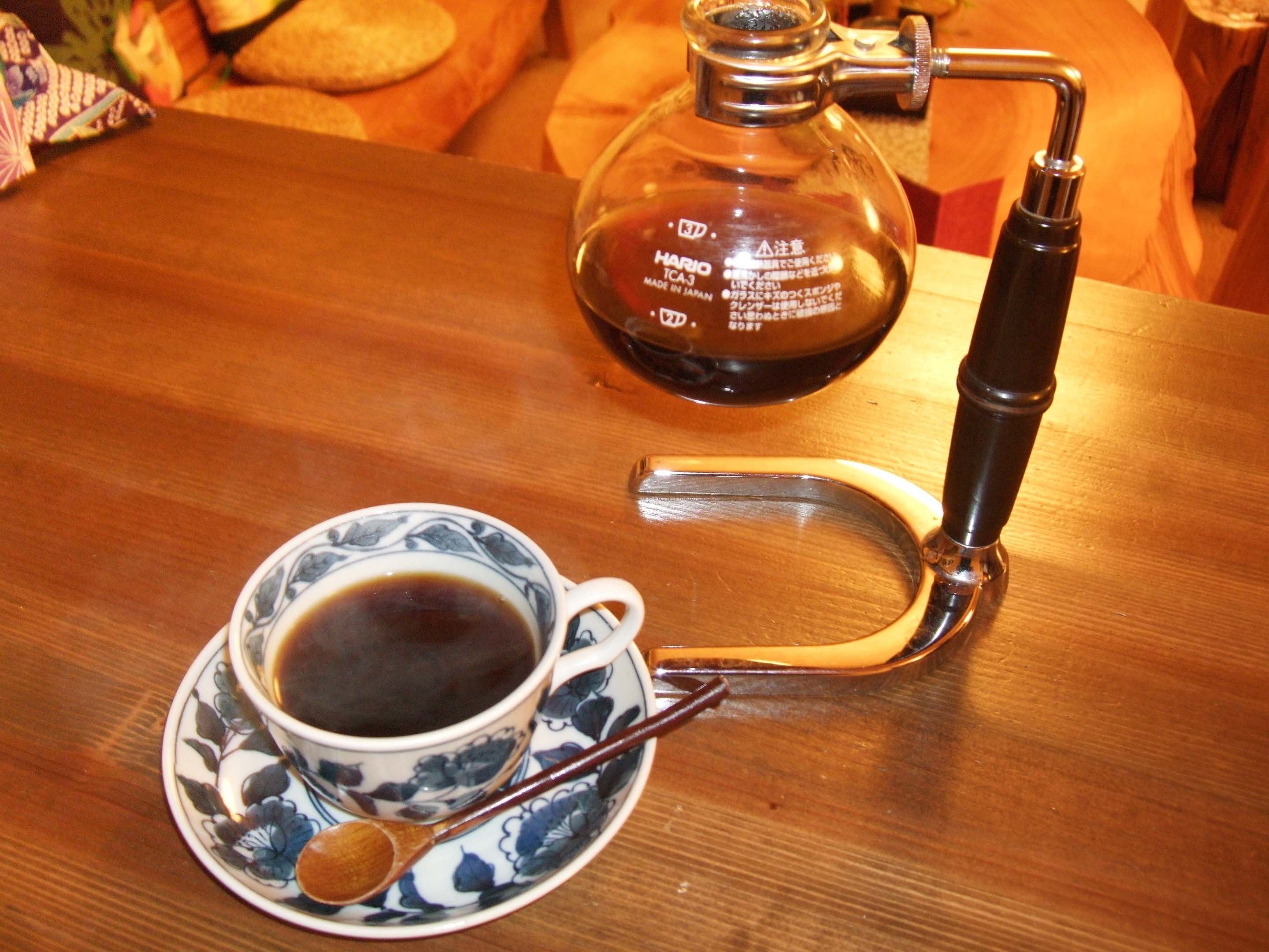A coffee maker with a glass carafe and a cup of coffee on a wooden table.