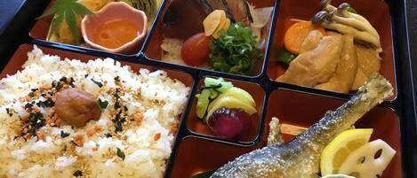 A bento box with rice, fish, vegetables, and a small bowl of green grapes.