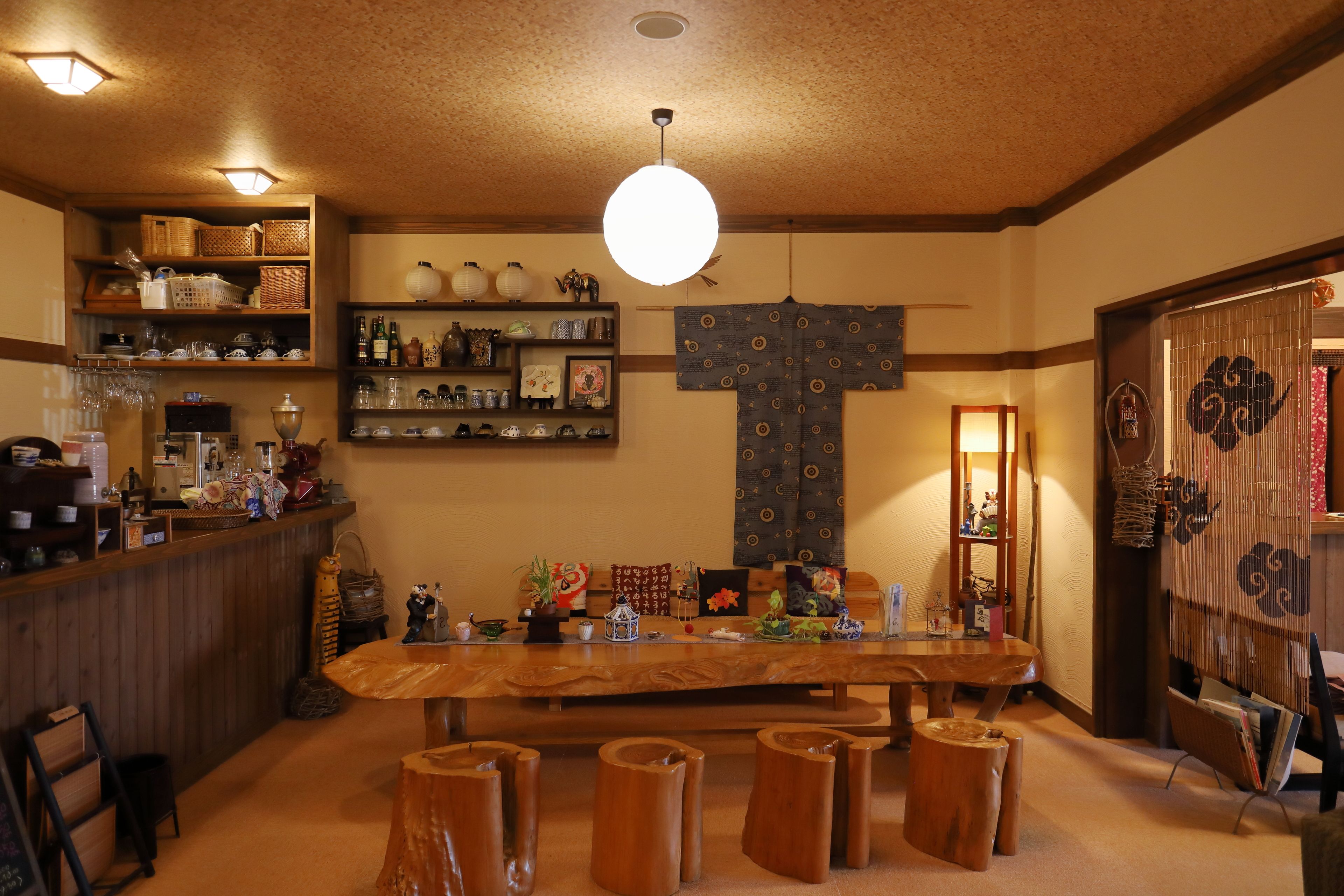 A traditional Japanese-style room with a wooden dining table, stools, and shelves with various items.