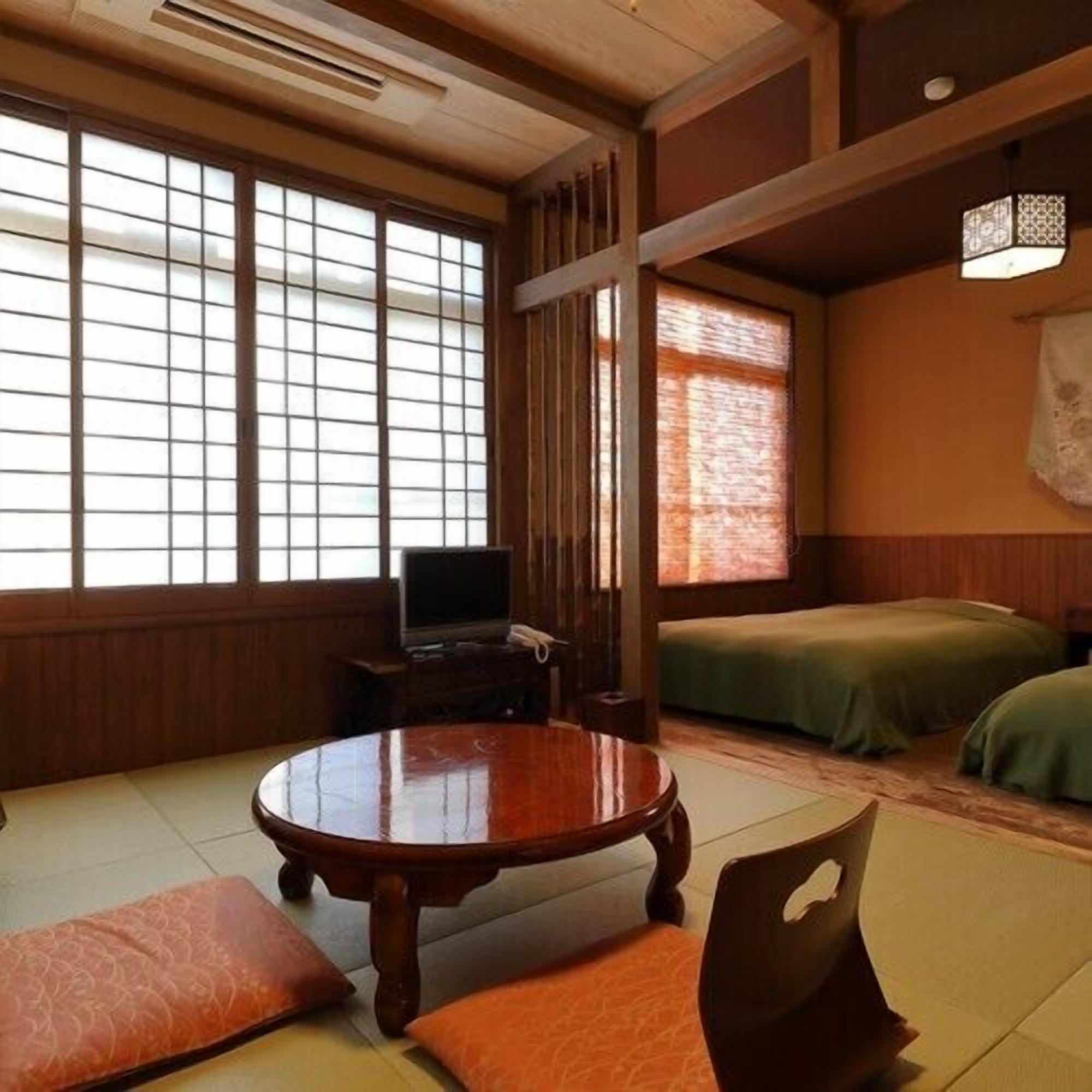 Une pièce de style japonais traditionnel, avec un sol recouvert de tatamis, une petite table en bois, un téléviseur et un lit avec une literie verte.