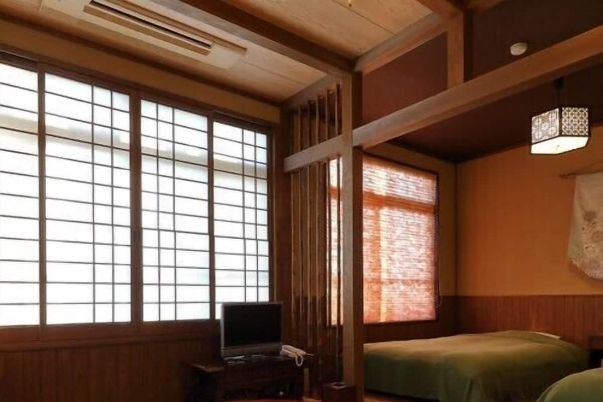 A traditional Japanese room with tatami flooring, a low wooden table, a television, and a bed with green bedding.