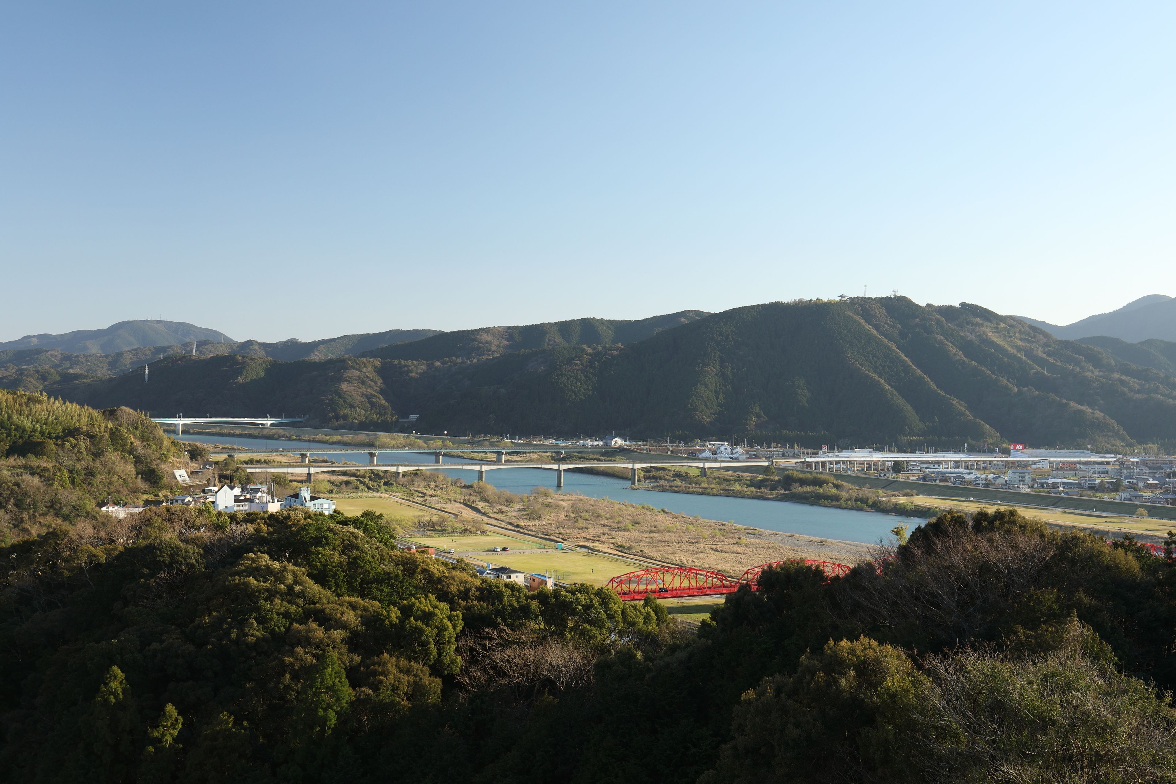 Un paysage pittoresque avec une rivière, des ponts et un pont ferroviaire rouge.