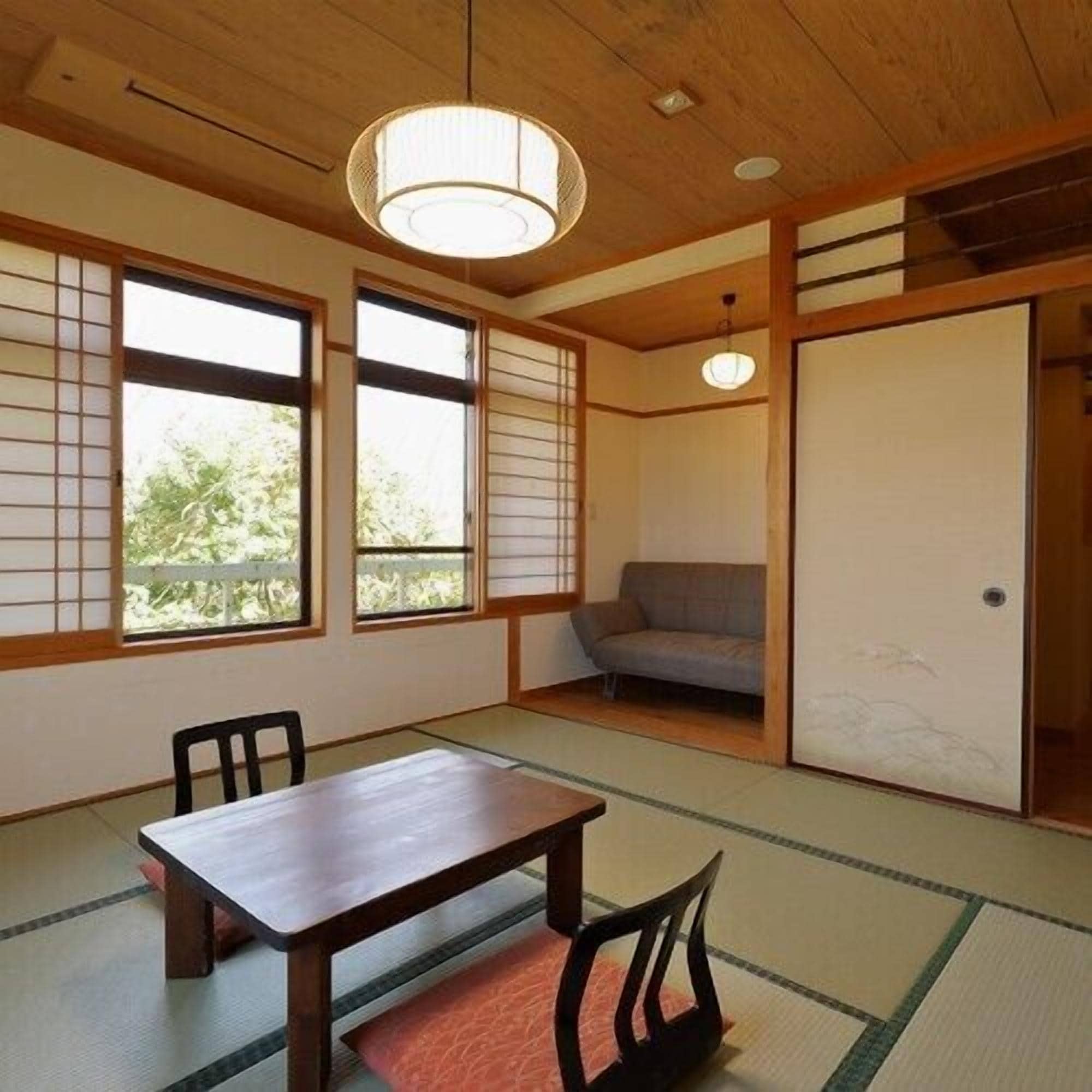 Une pièce de style japonais traditionnel, avec un sol recouvert de tatamis, une table basse, des chaises, un canapé et des portes coulissantes.