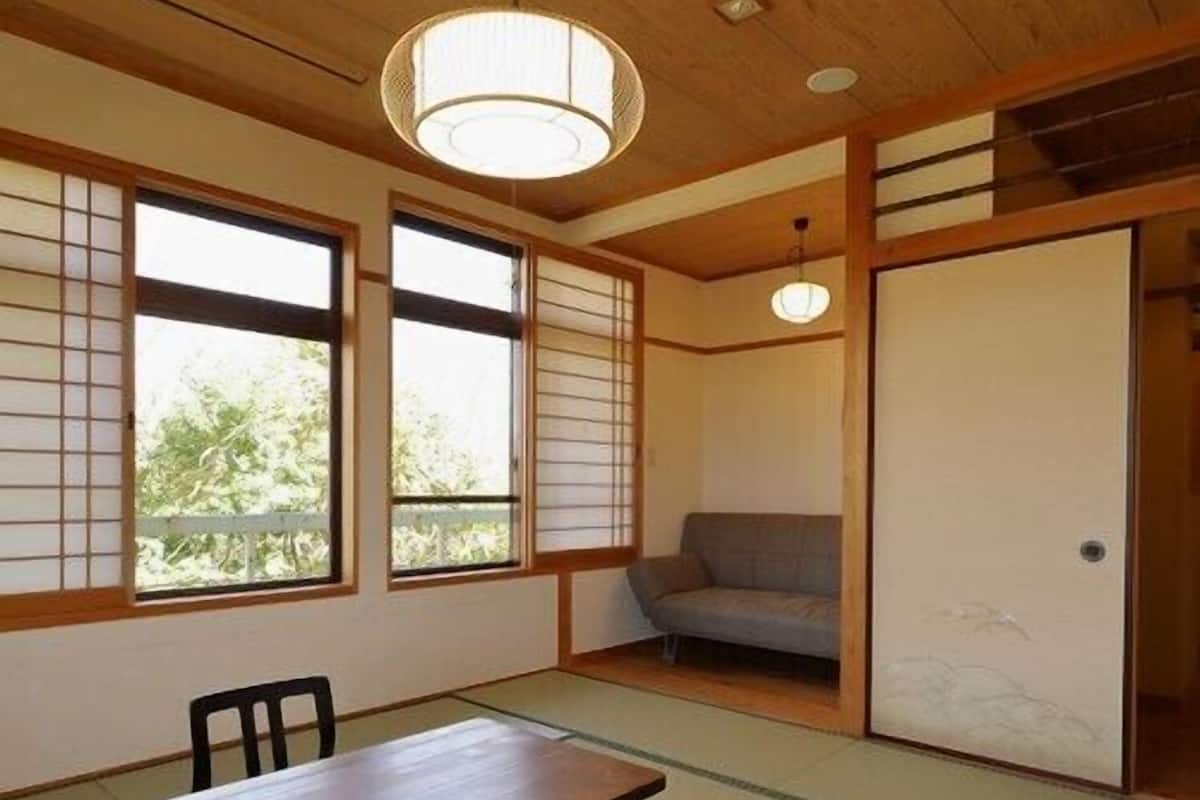 A traditional Japanese room with tatami flooring, a low table, chairs, a sofa, and sliding doors.