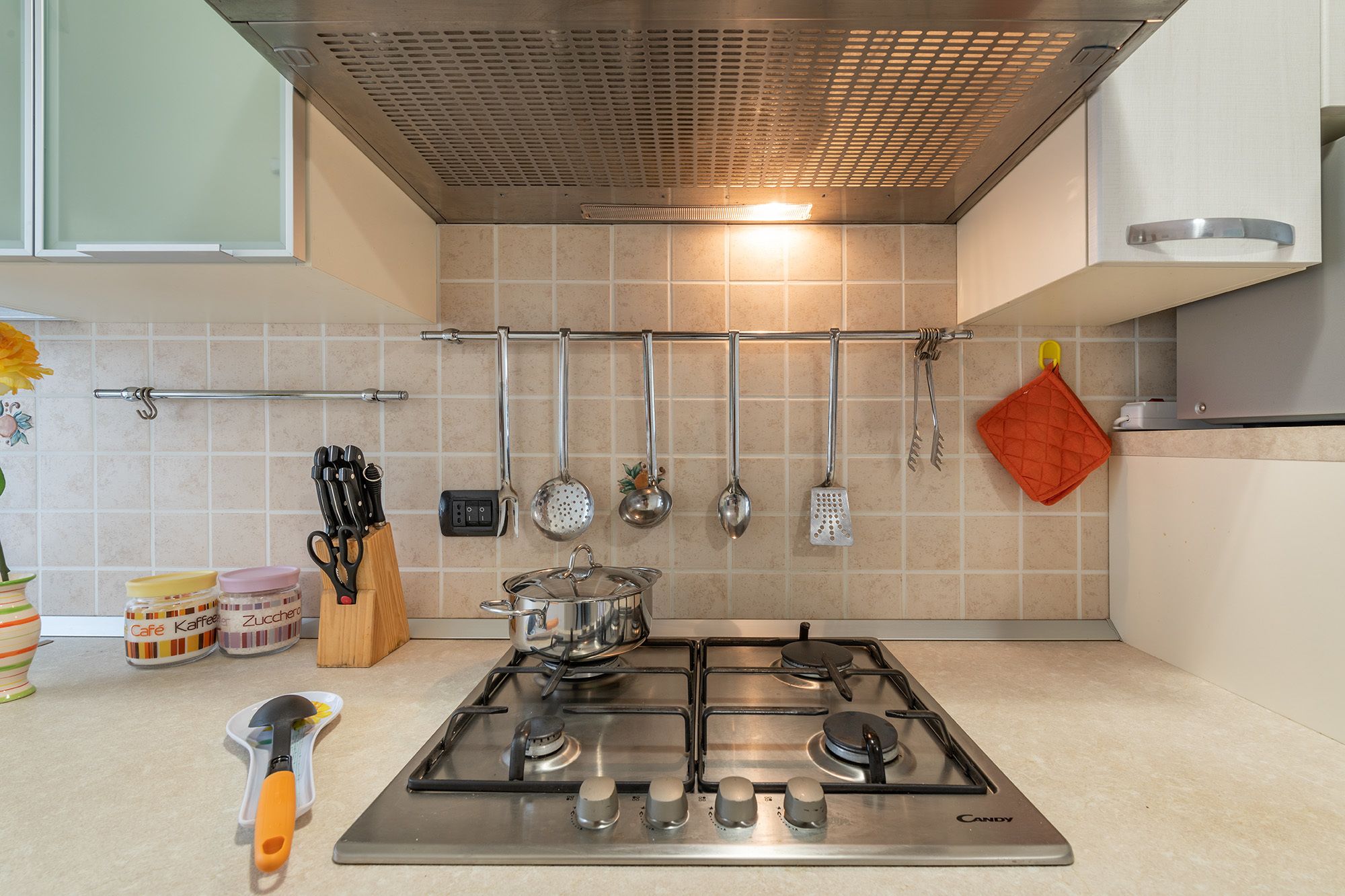 Cozinha com fogão a gás, utensílios pendurados e painel de azulejos.