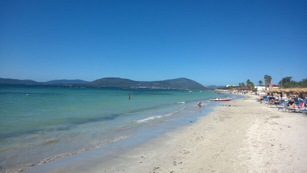 A beach with clear turquoise water, a sandy shore, and a few people.