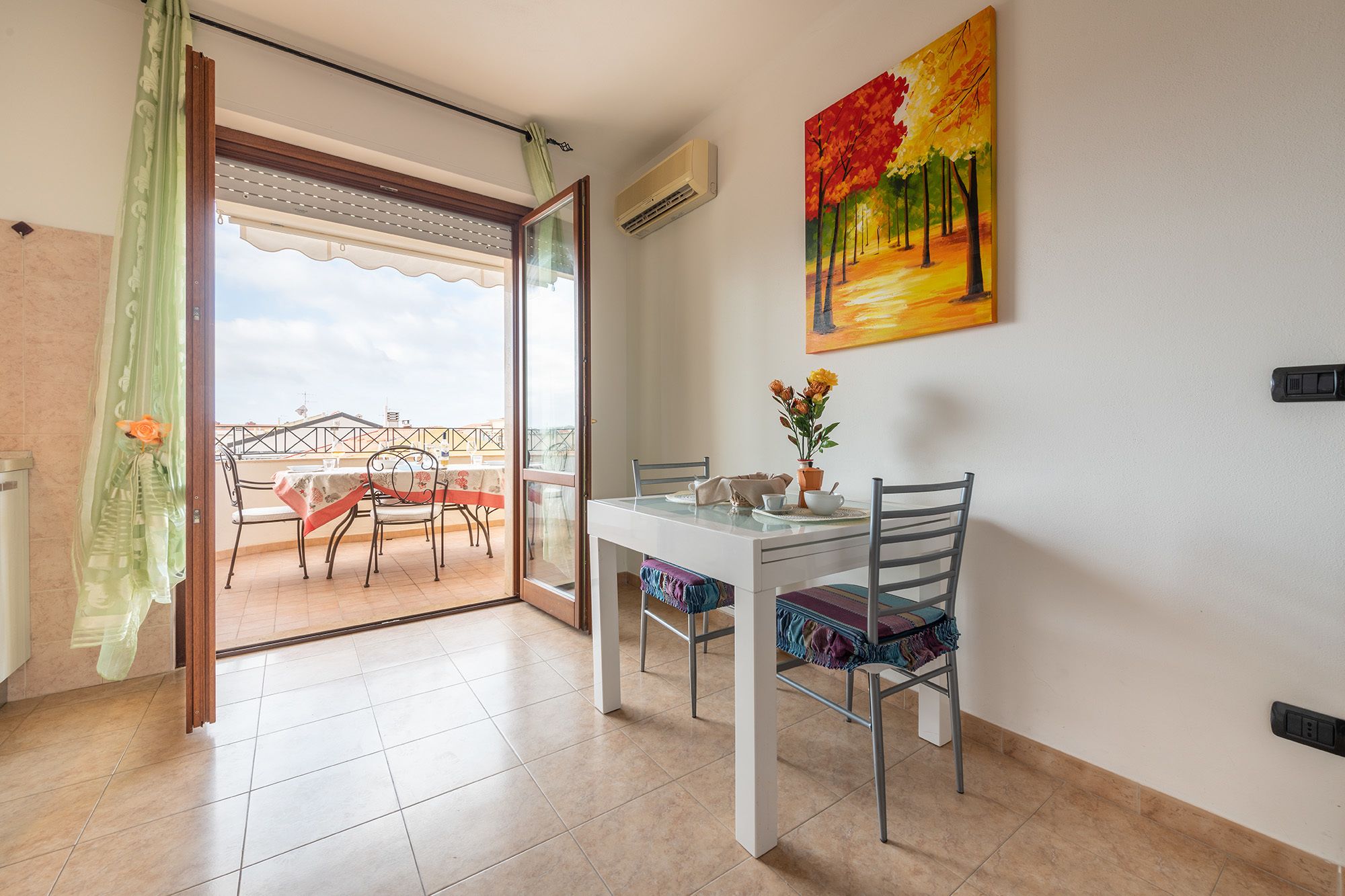 Uma sala de jantar com mesa e cadeiras, um quadro na parede e vista para uma varanda através de uma porta de vidro.