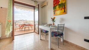 A dining area with a table and chairs, a painting on the wall, and a view through a glass door to an outdoor balcony.