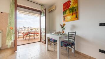 Uma sala de jantar com mesa e cadeiras, um quadro na parede e vista para uma varanda através de uma porta de vidro.