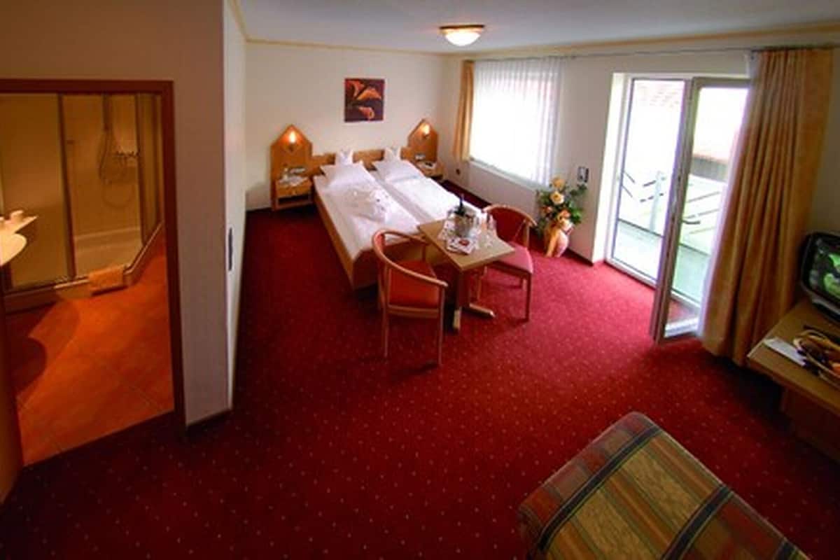 A hotel room with a bed, a dining table with chairs, a TV, and a balcony with a view.