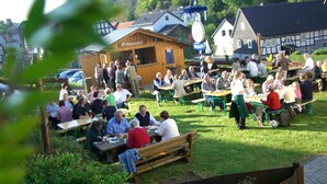 An outdoor gathering with people seated at tables and benches, surrounded by buildings with traditional architecture. - Haus Wiesengrund (Hallenberg)