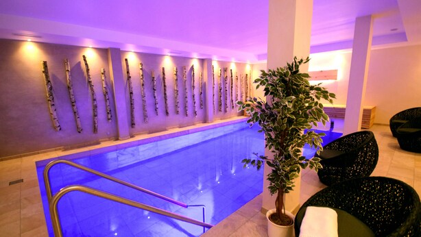 A modern indoor pool area with a long, narrow pool, a staircase leading to the pool, and several black chairs with white cushions. - Haus Wiesengrund (Hallenberg)