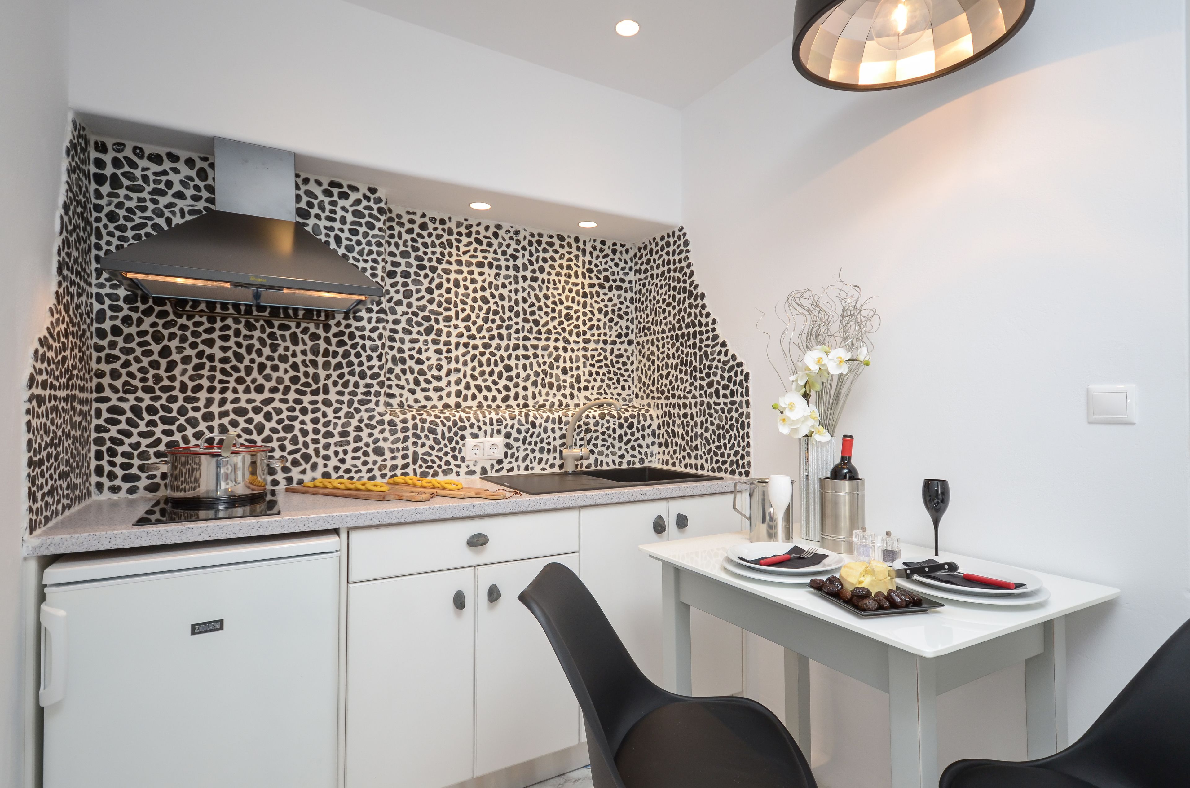 A modern kitchen with a unique stone backsplash, a built-in stove, and a dining area with a white table and black chairs.