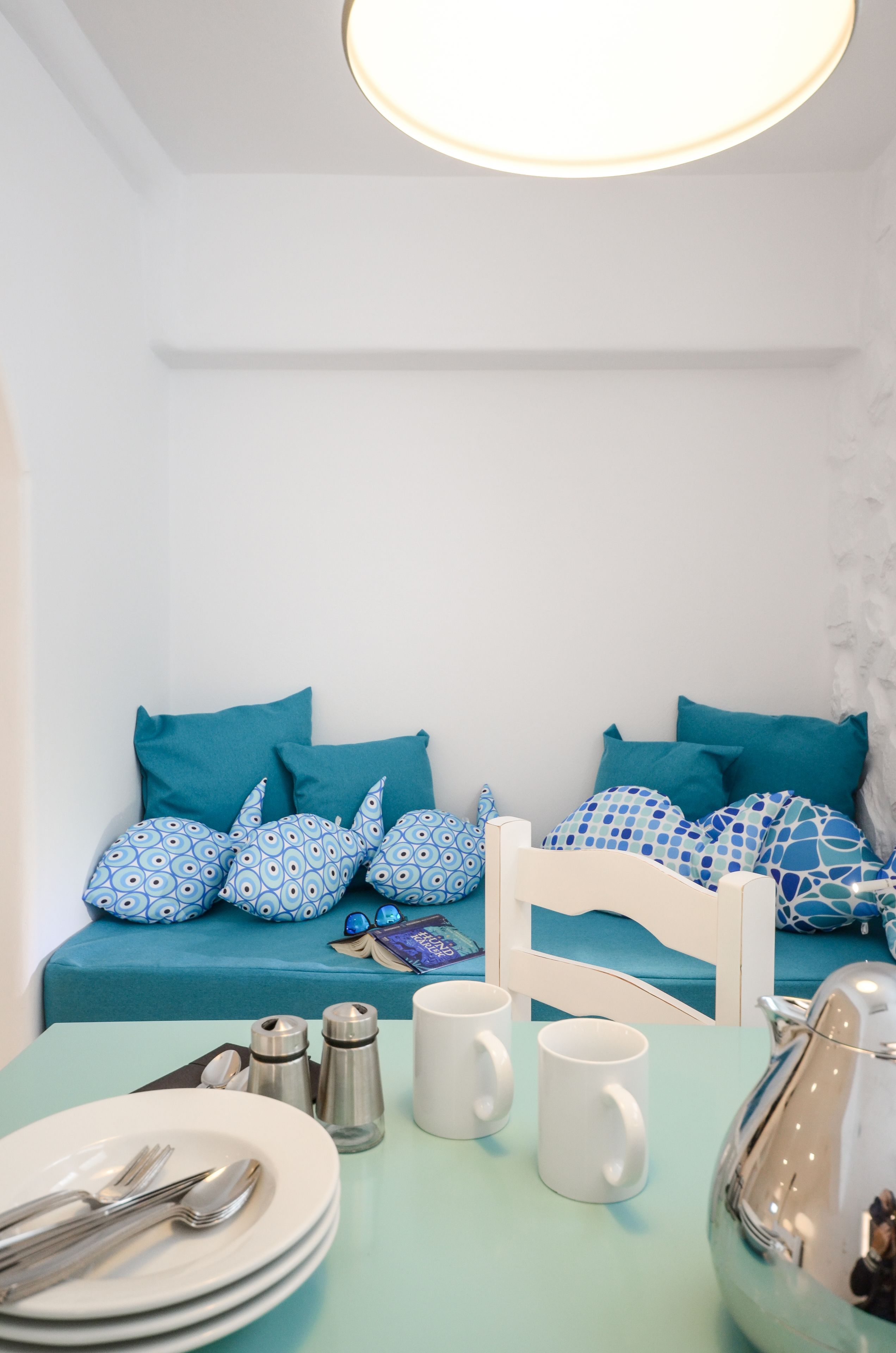 A neatly arranged dining area with a table set for two, a bed with teal bedding, and a white wall.