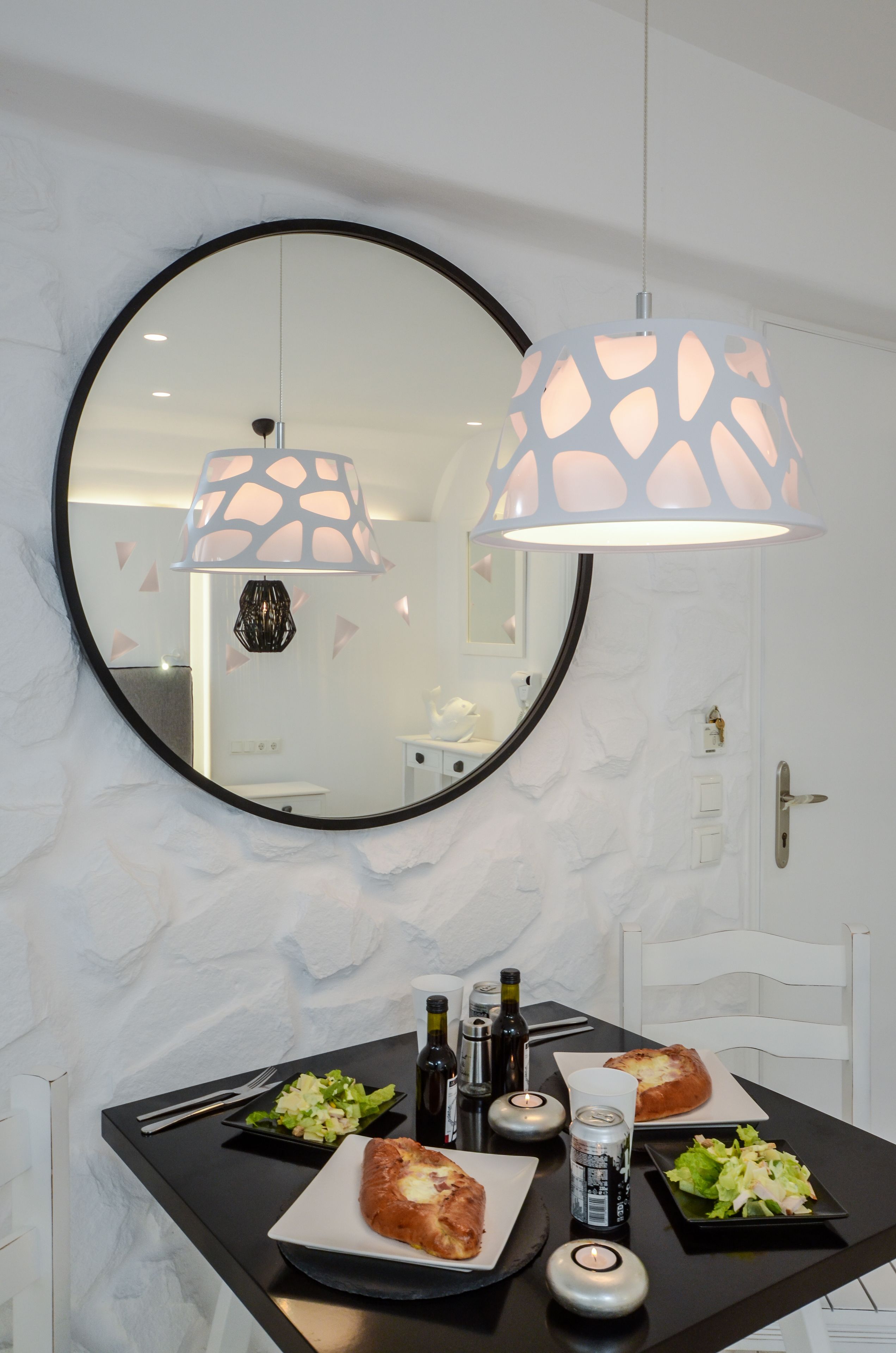 A bathroom with a round mirror, two pendant lights, and a sink with a black countertop.