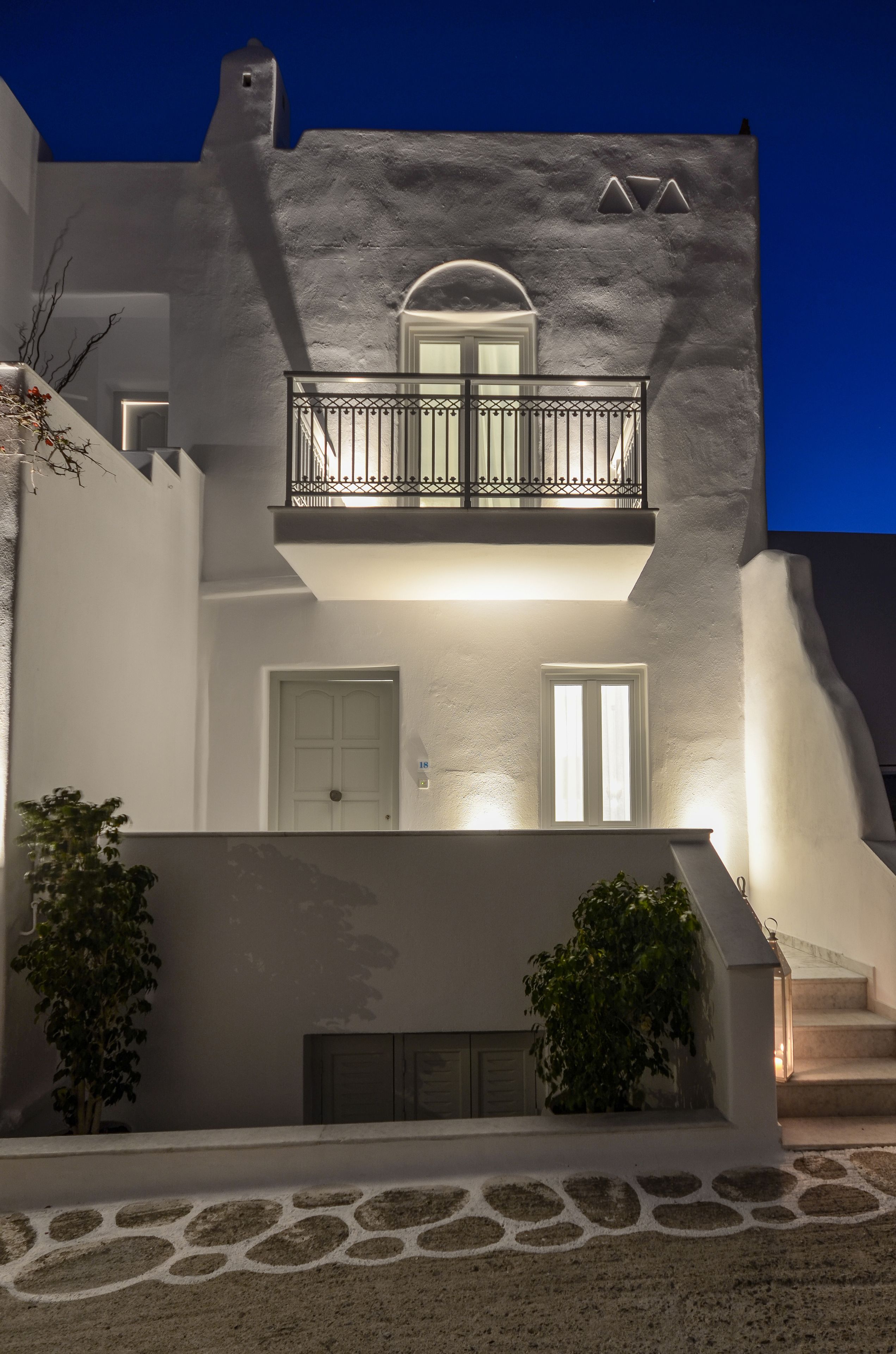Un edificio de dos pisos con un balcón, una puerta blanca y una ventana pequeña.
