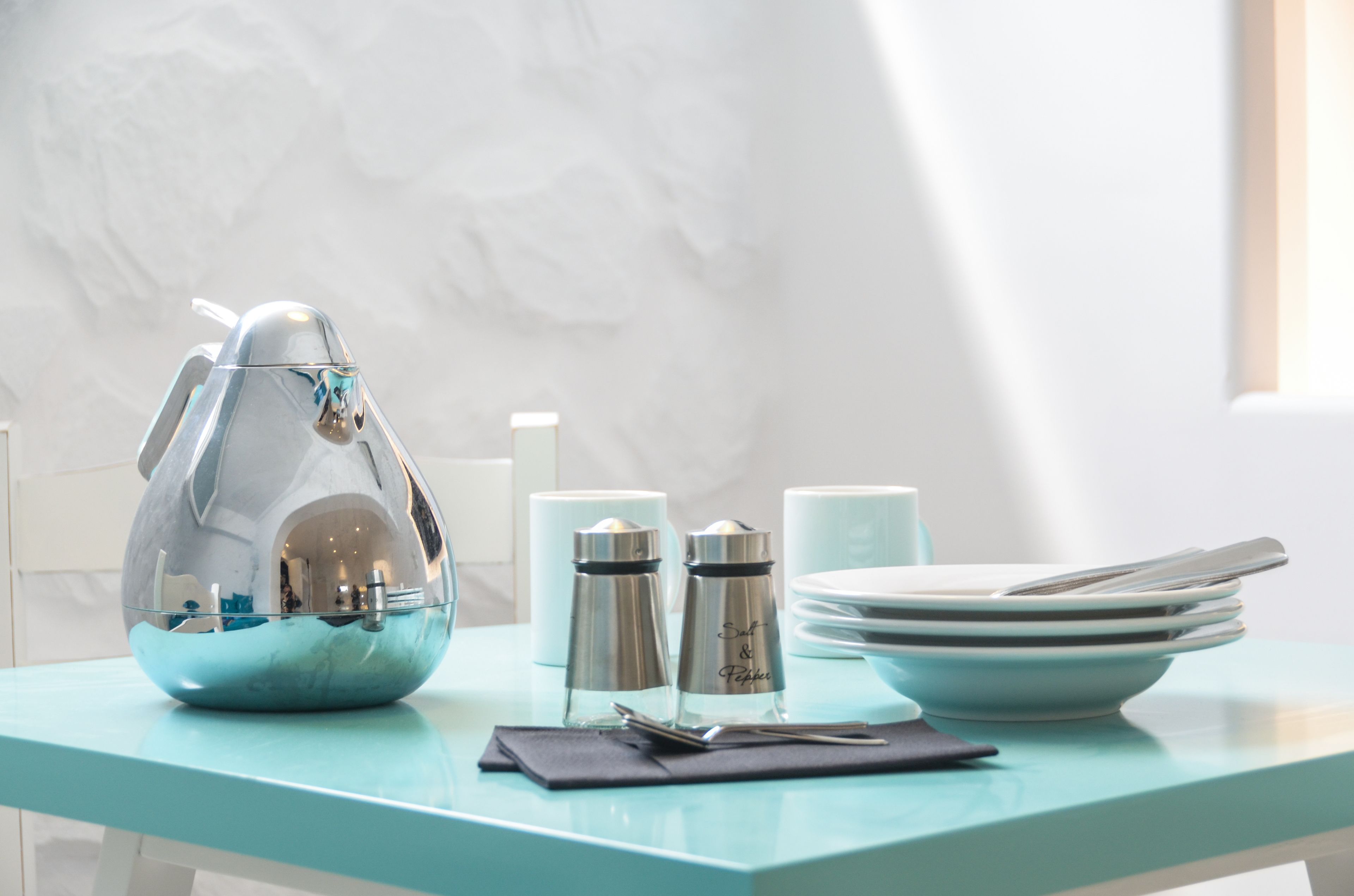 A table with a decorative egg-shaped container, salt and pepper shakers, a stack of plates, and a napkin.