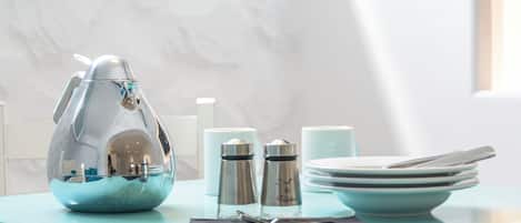 A table with a decorative egg-shaped container, salt and pepper shakers, a stack of plates, and a napkin.