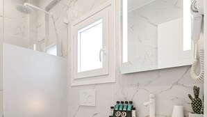 A modern bathroom with a white toilet, a shower, a marble-tiled floor, a white sink with a mirror above it, and a small cactus plant on the counter. - Naxos Evilion (Naxos)
