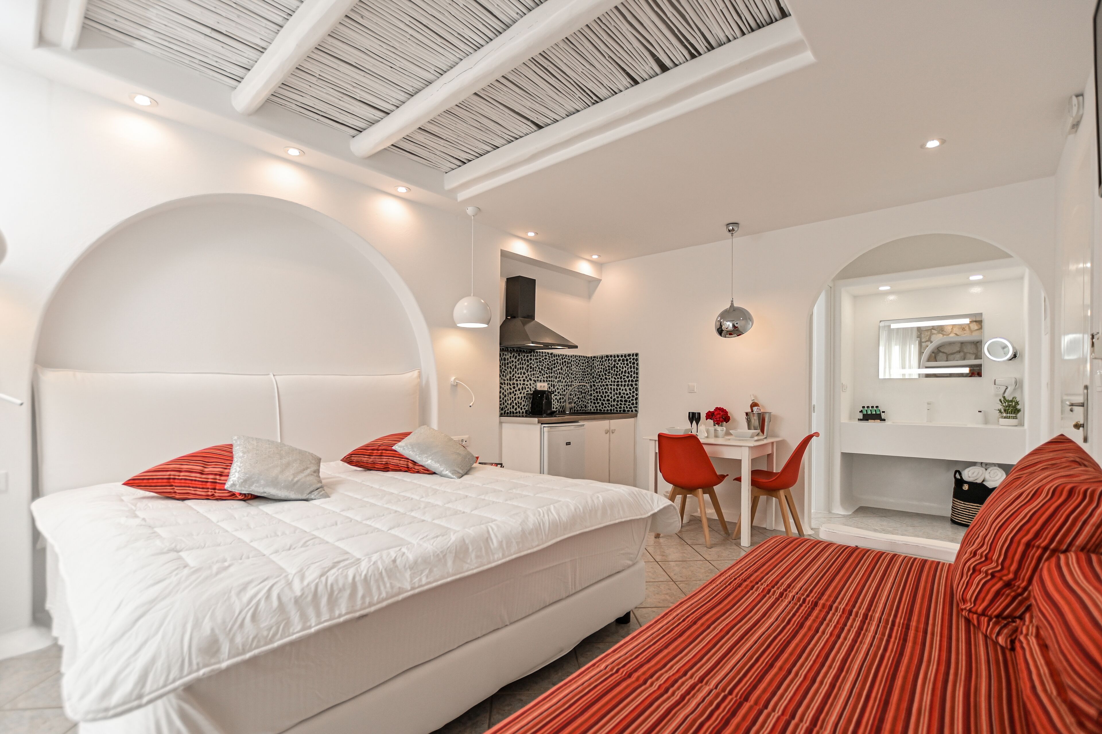 A modern bedroom with a large bed, a desk, and a kitchenette.