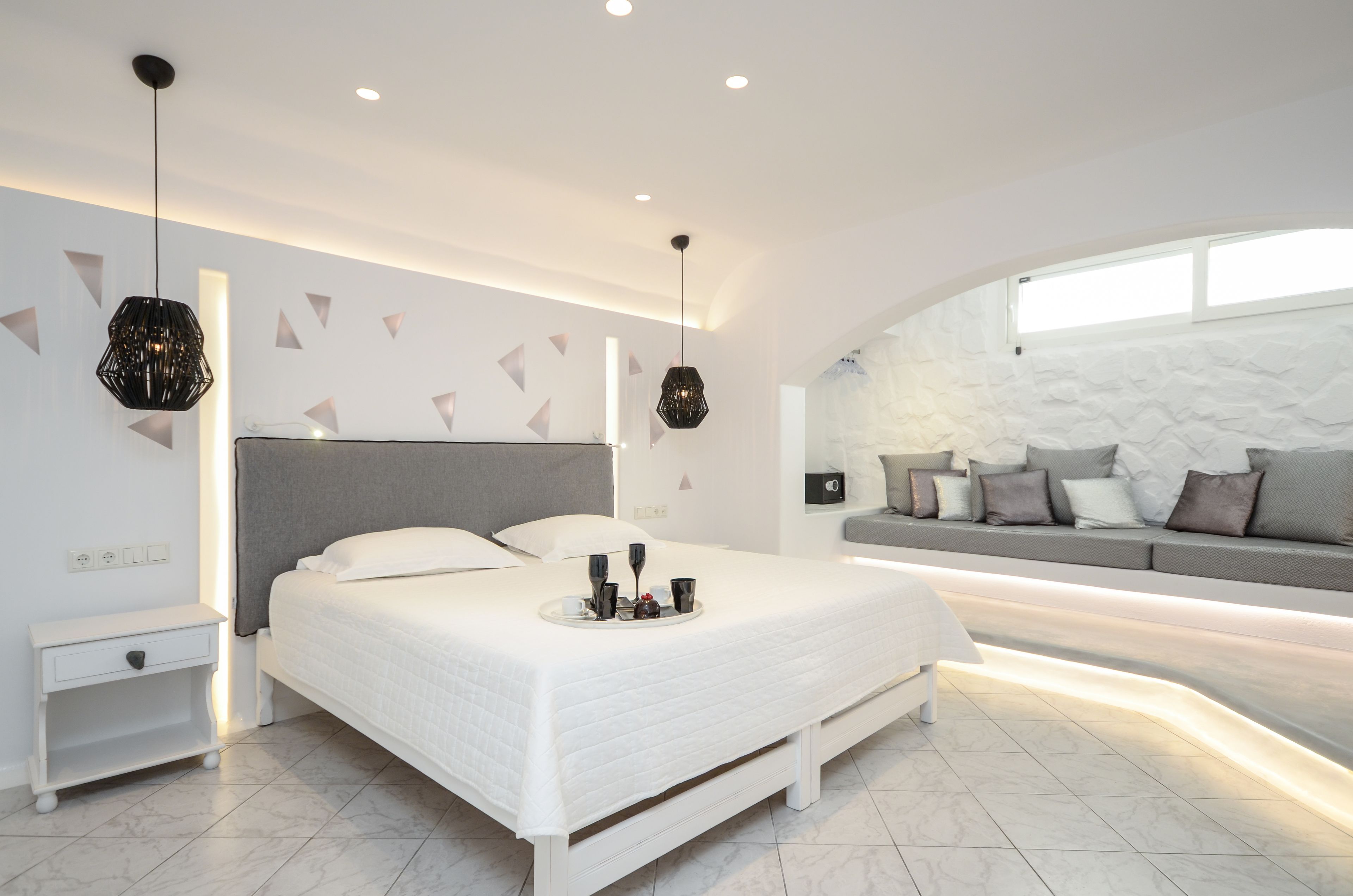 A modern bedroom with a large bed, bedside tables, a sofa, and a stone accent wall.
