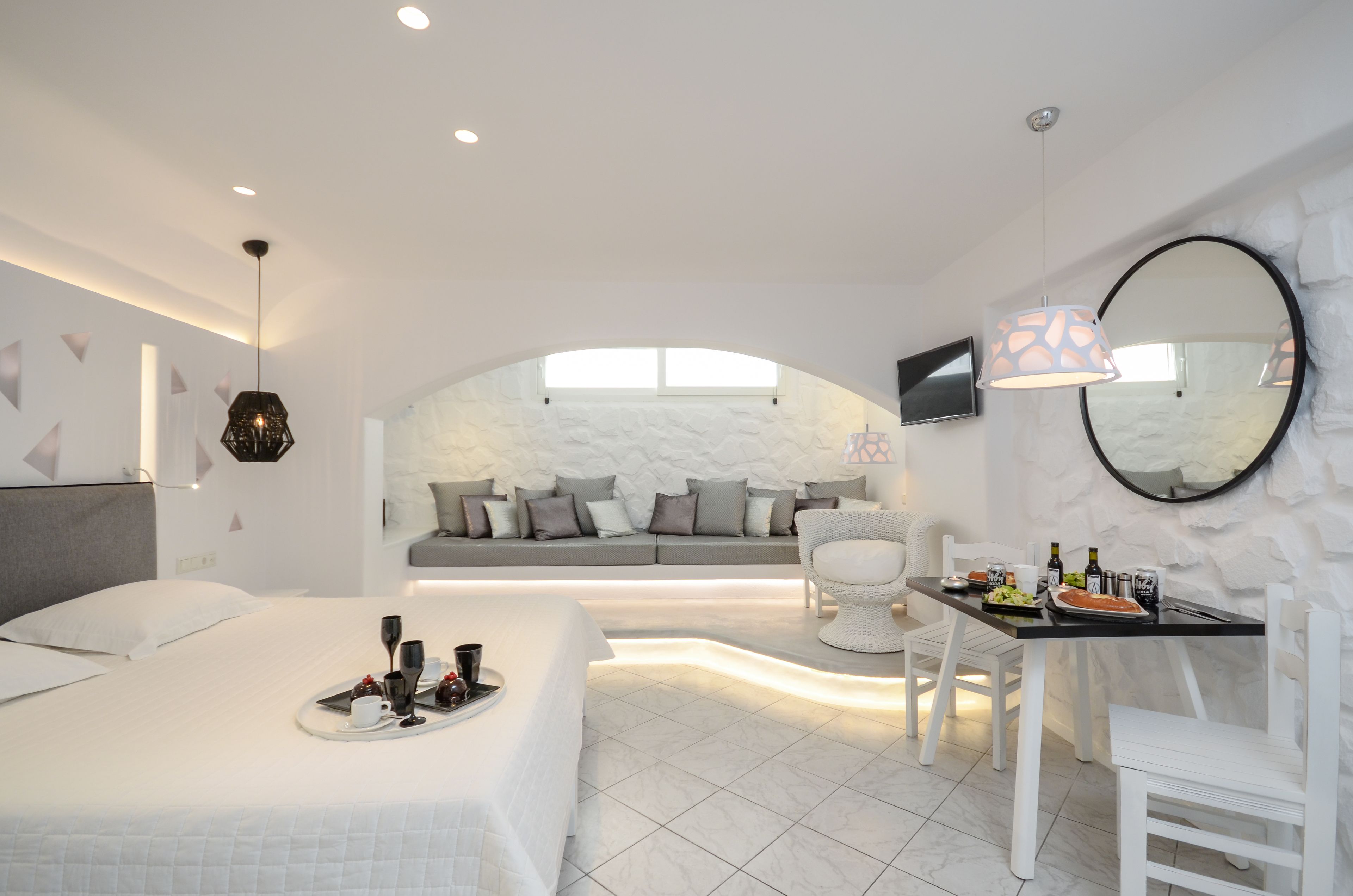 A modern hotel room with a bed, breakfast tray, seating area, and a stone accent wall.