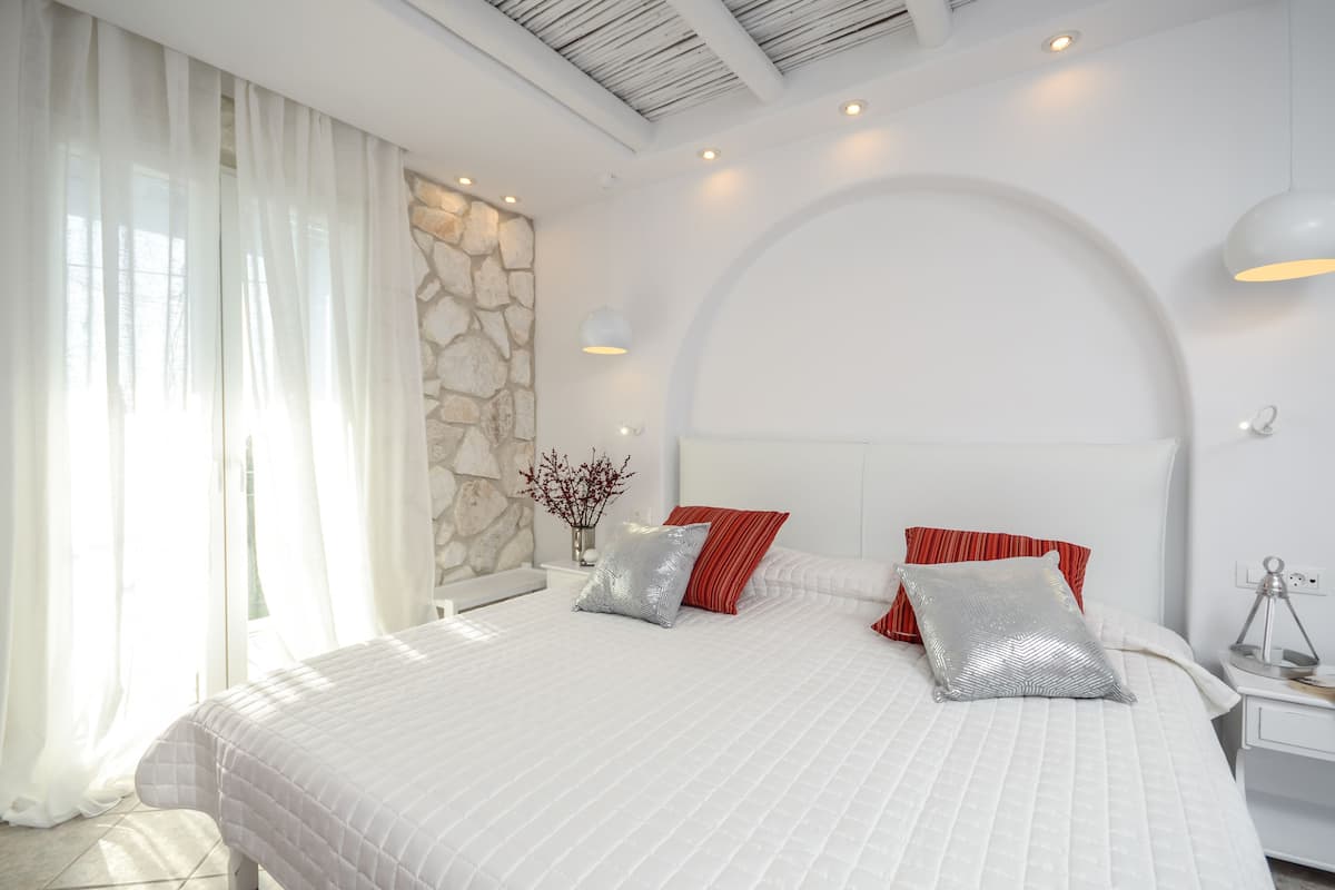 Ein modernes Schlafzimmer mit einem großen Bett, weißer Bettwäsche und einer Wand mit Steinverkleidung.
