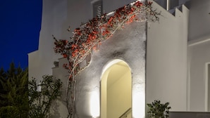 Un edificio moderno con fachada blanca, un camino de piedra que lleva a unas escaleras y una entrada bien iluminada.