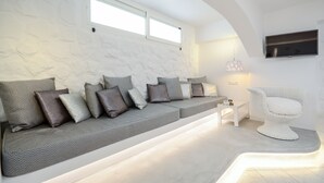 Una sala de estar moderna con un sofá gris, paredes blancas, un televisor de pantalla plana y una silla blanca.