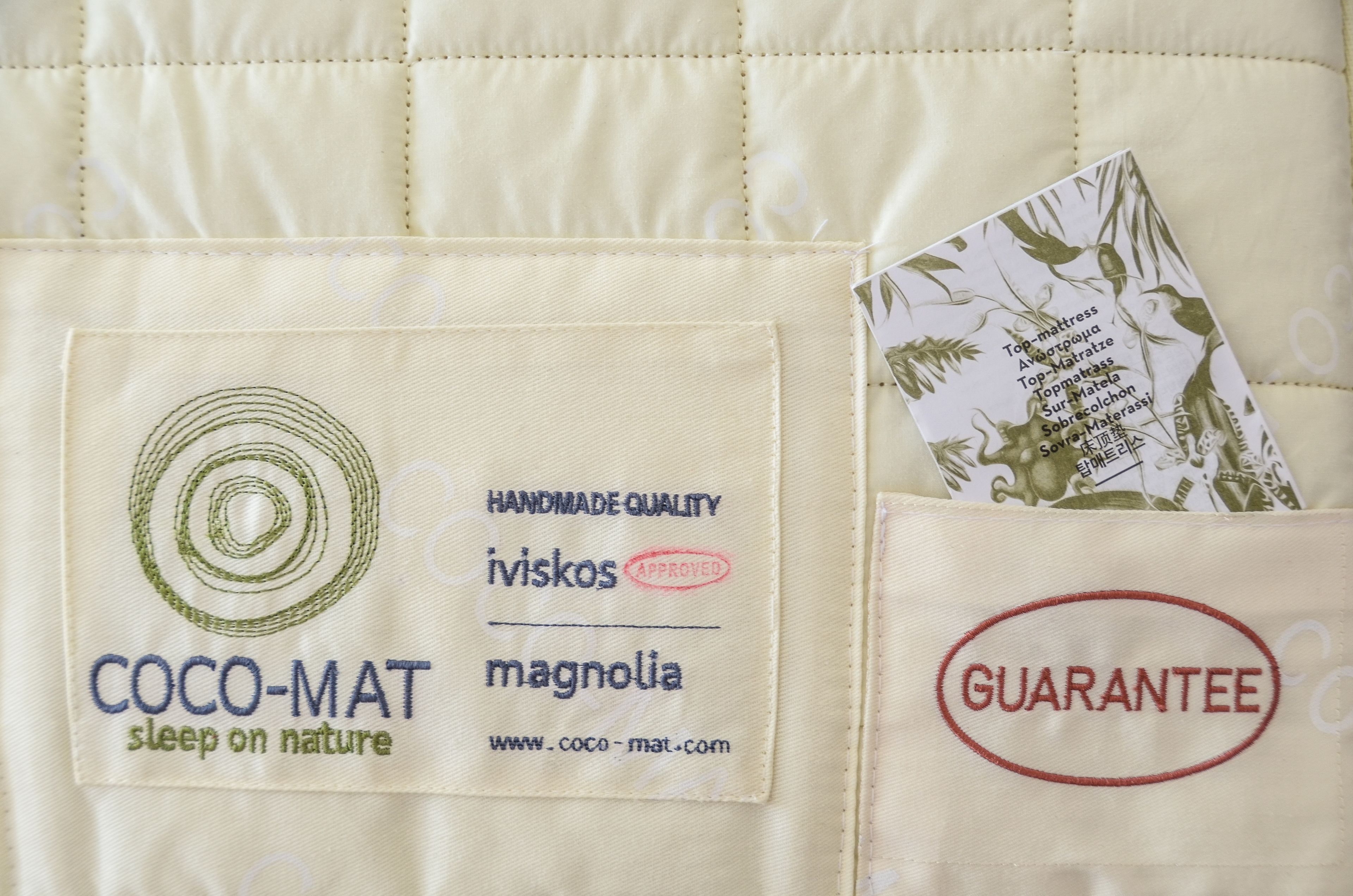 A close-up of a bed with a label indicating 'COCO-MAT sleep on nature' and a 'GUARANTEE' tag.
